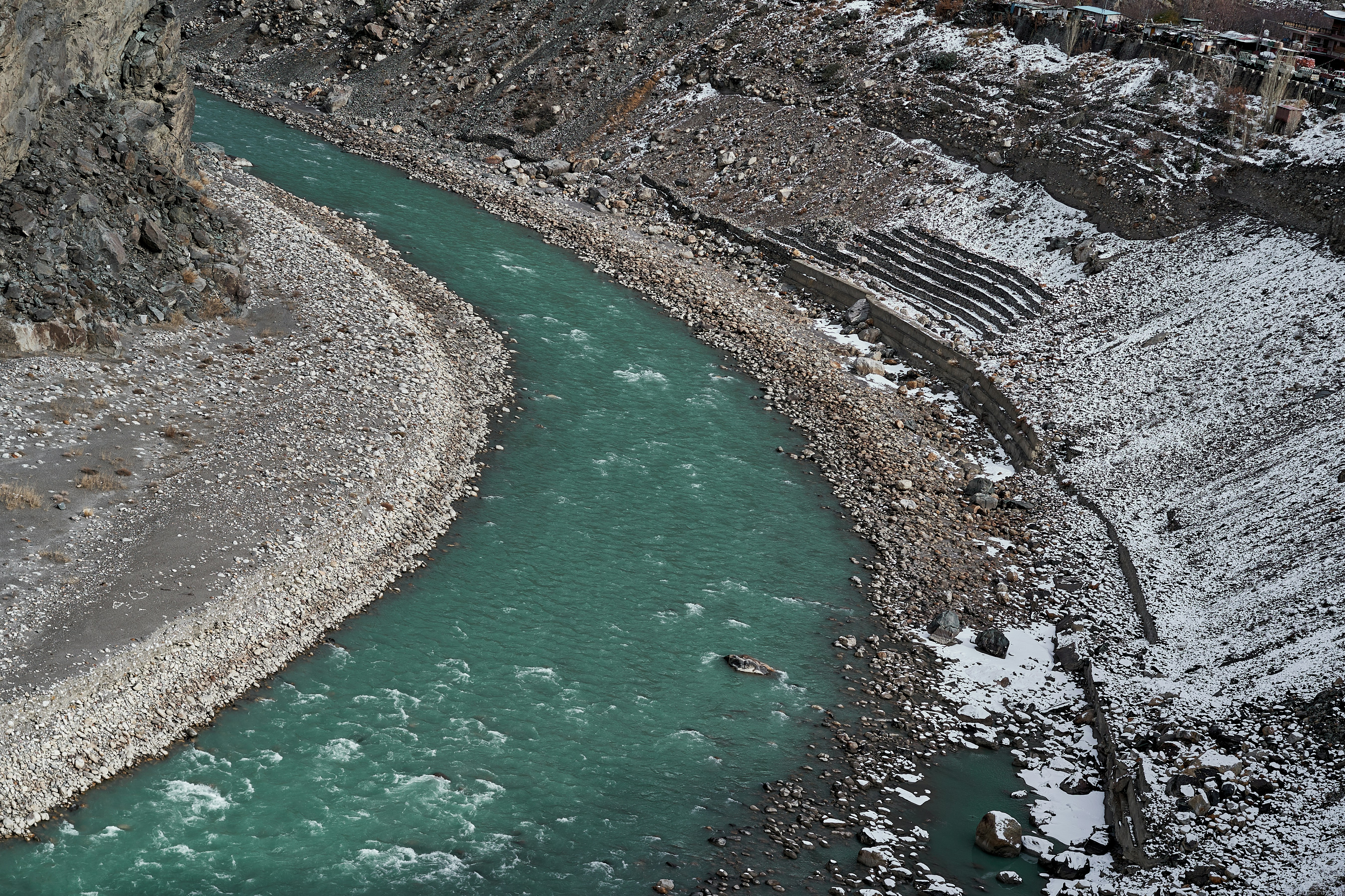 A turquoise river flowing through a rocky valley with snow on the banks