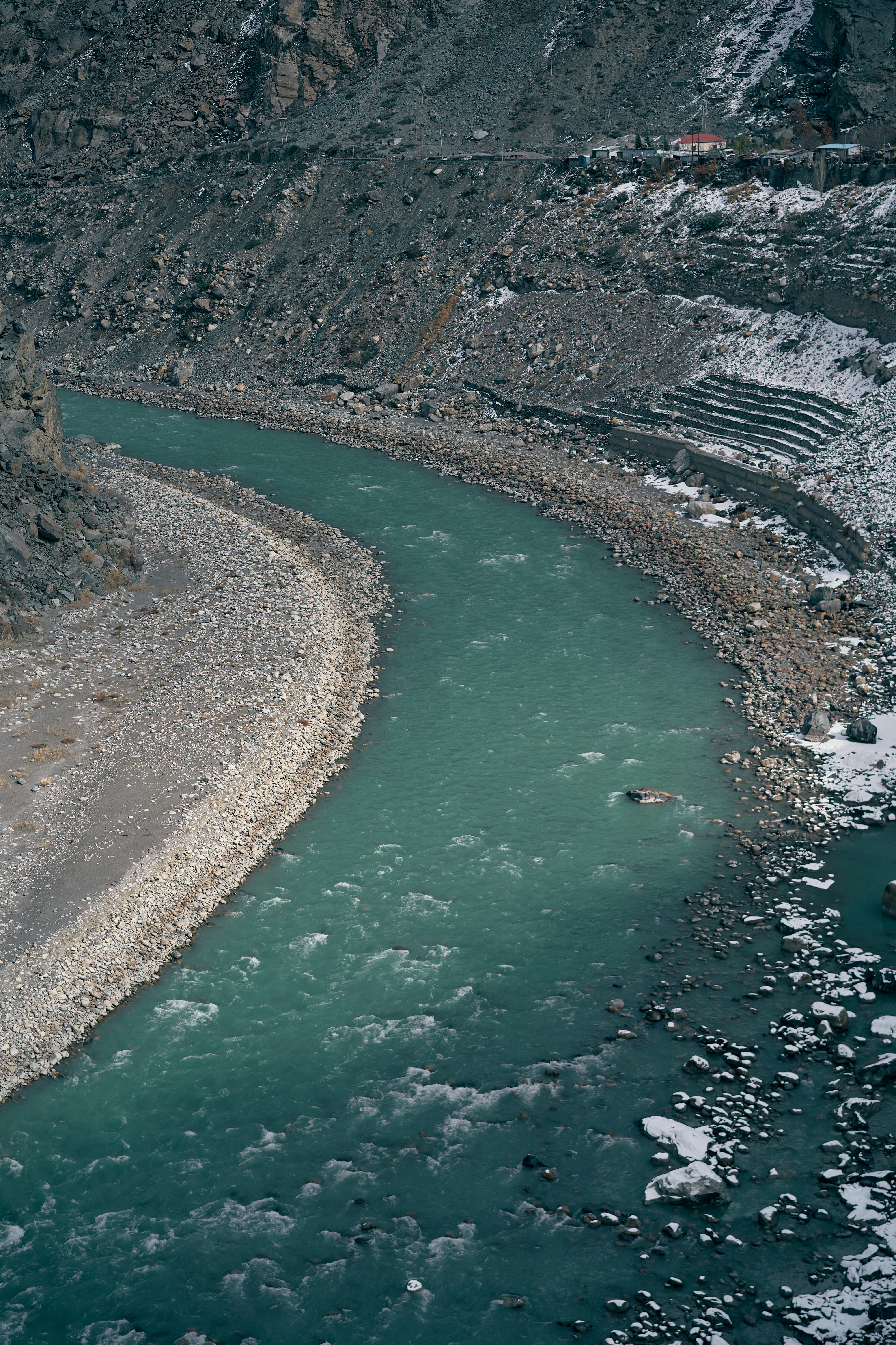 A turquoise river flowing through a rocky valley with patches of snow