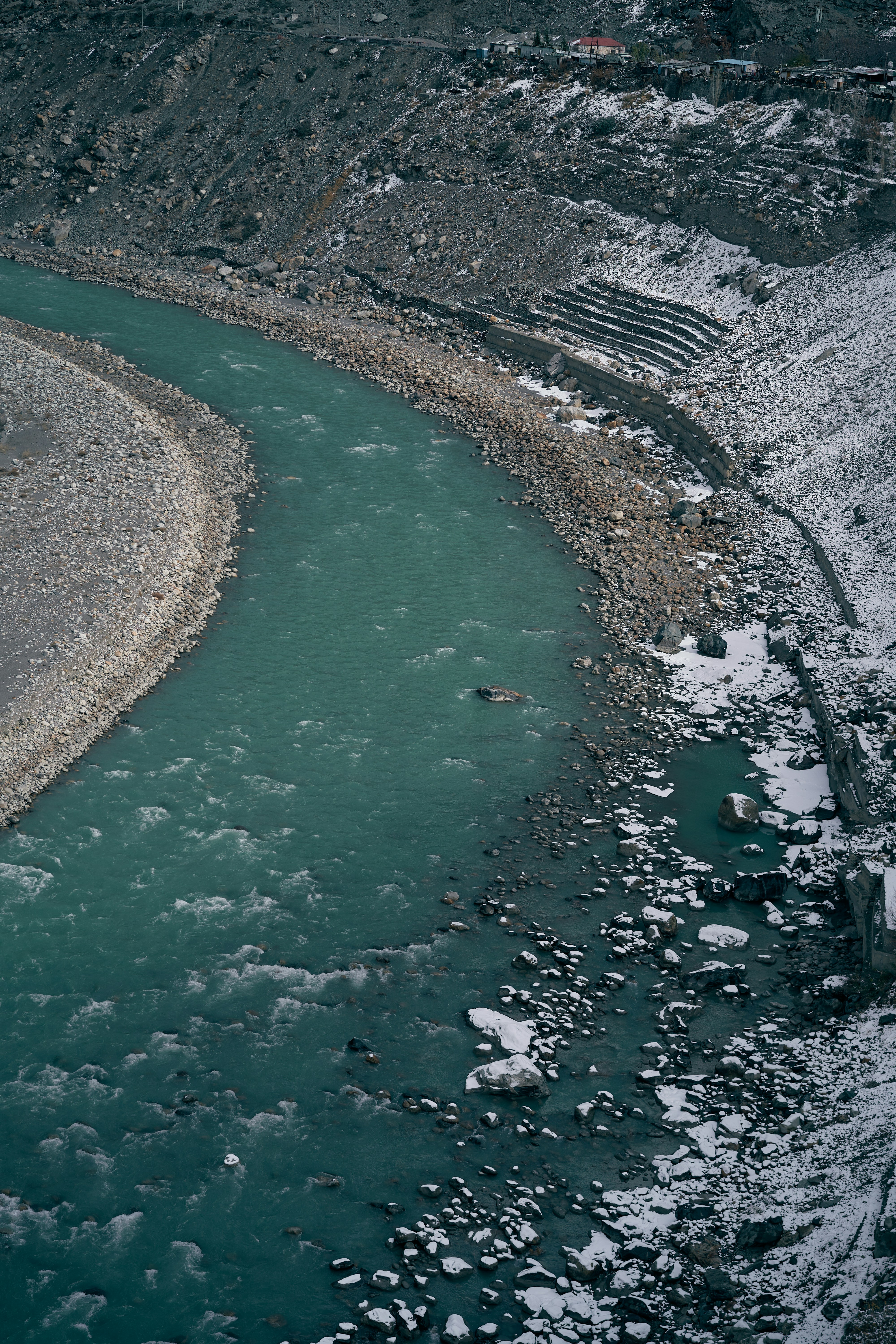 A turquoise river flowing through a rocky valley with patches of snow