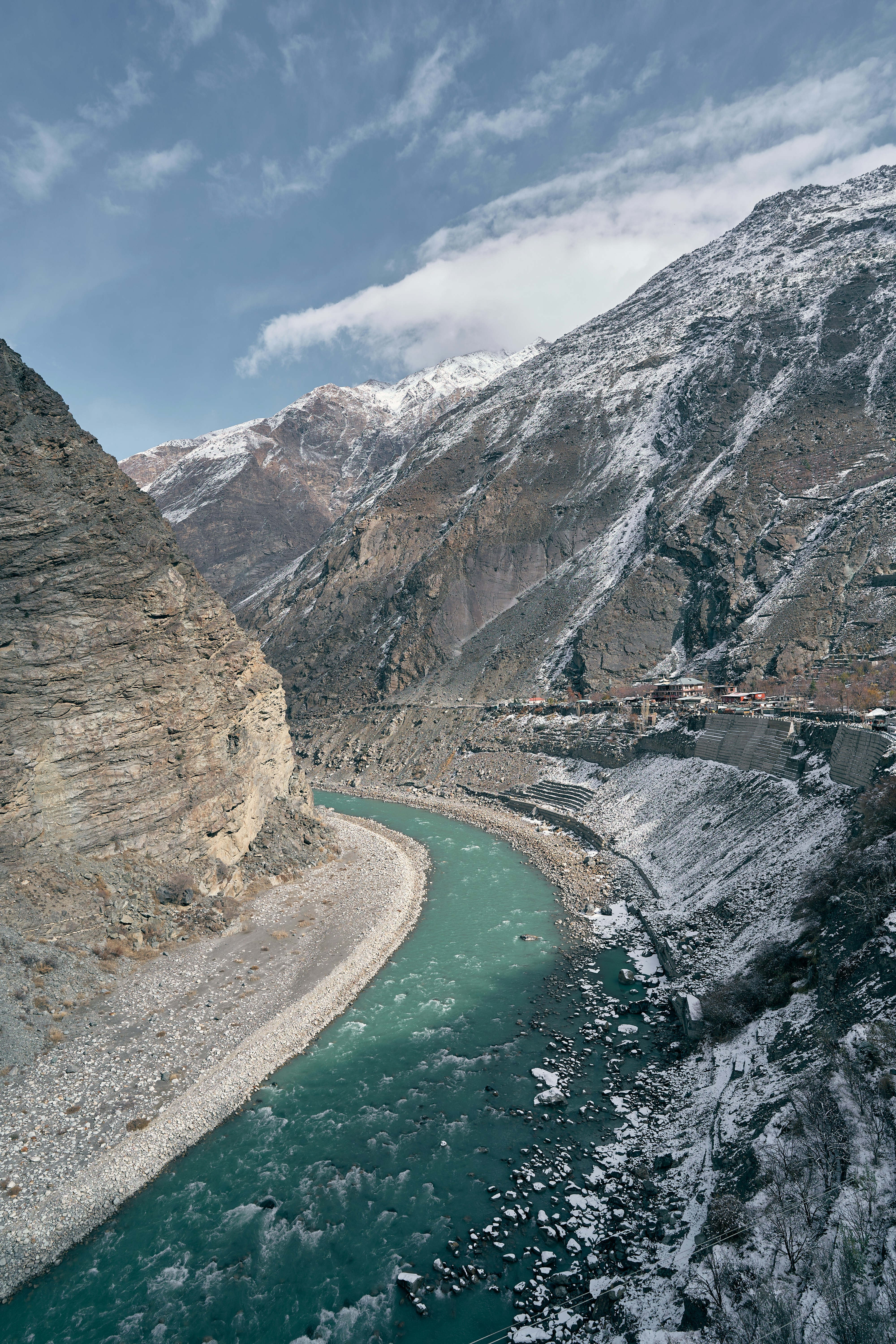 A turquoise river flowing through a deep valley with snow-dusted mountains and a village