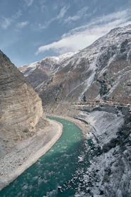 A turquoise river flowing through a deep valley with snow-dusted mountains and a village