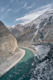 A turquoise river flowing through a deep valley with snow-dusted mountains and a village
