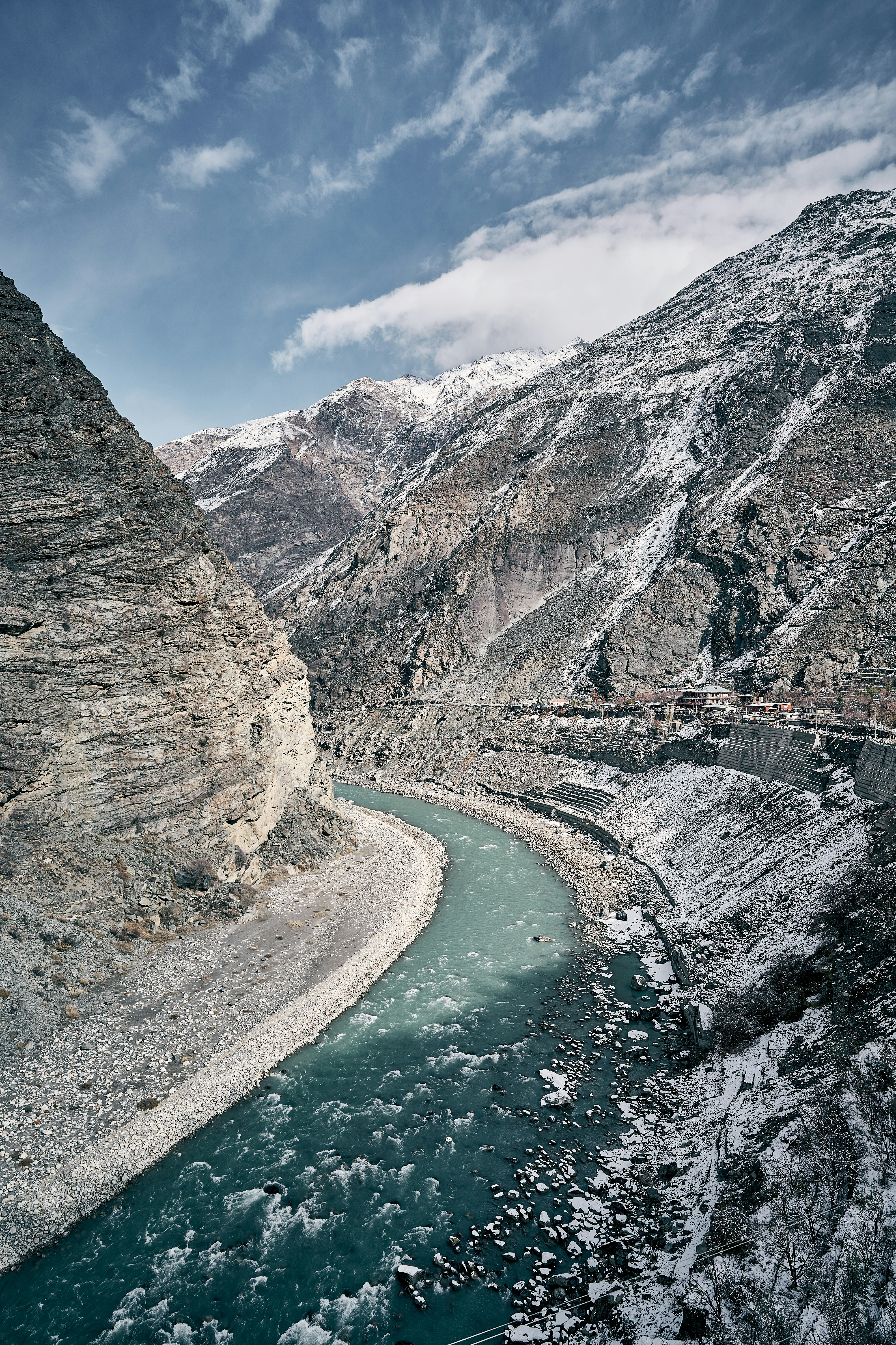 A turquoise river flowing through a deep valley between snow-dusted rocky mountains
