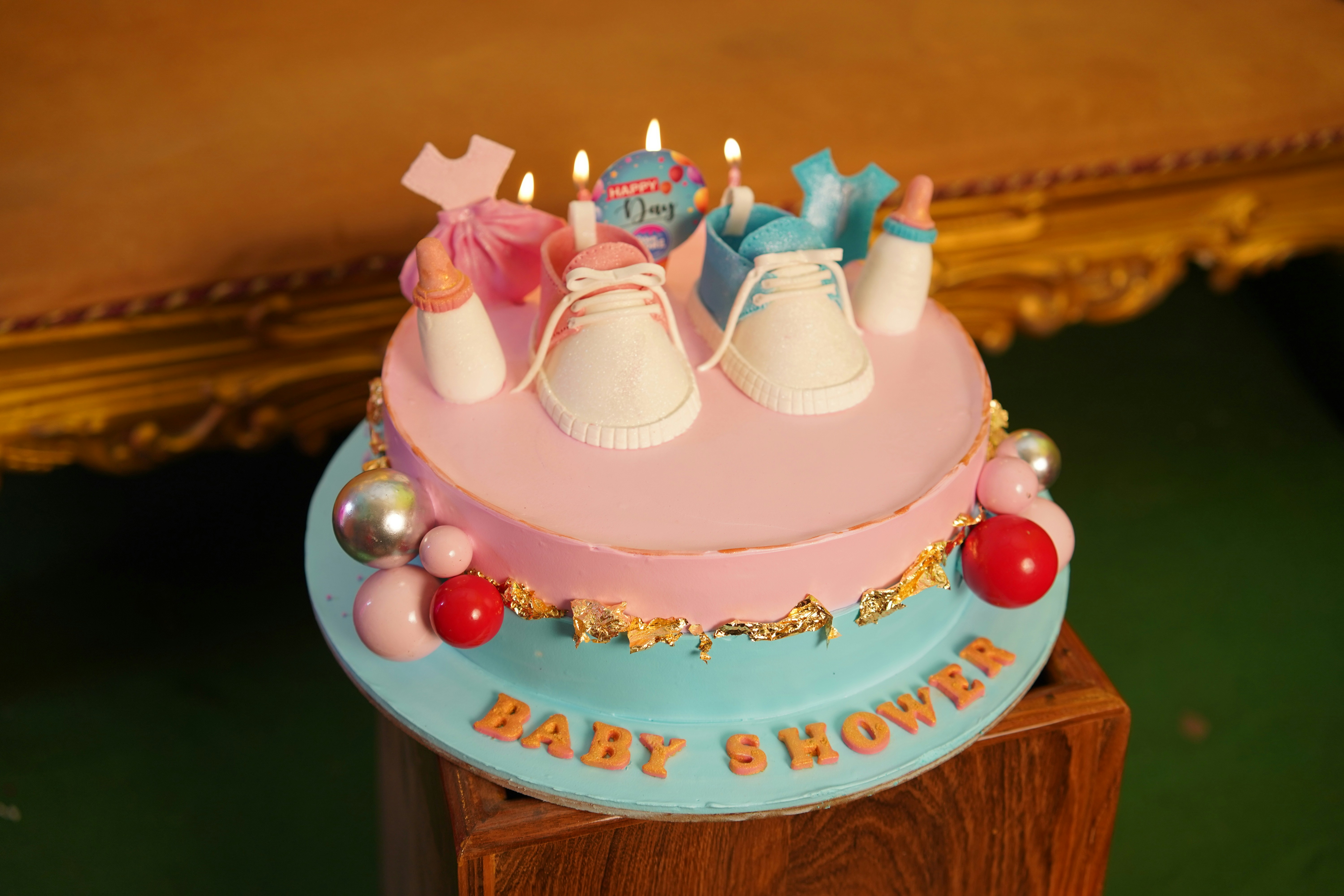 A baby shower cake with pink and blue frosting, baby shoes, and lit candles