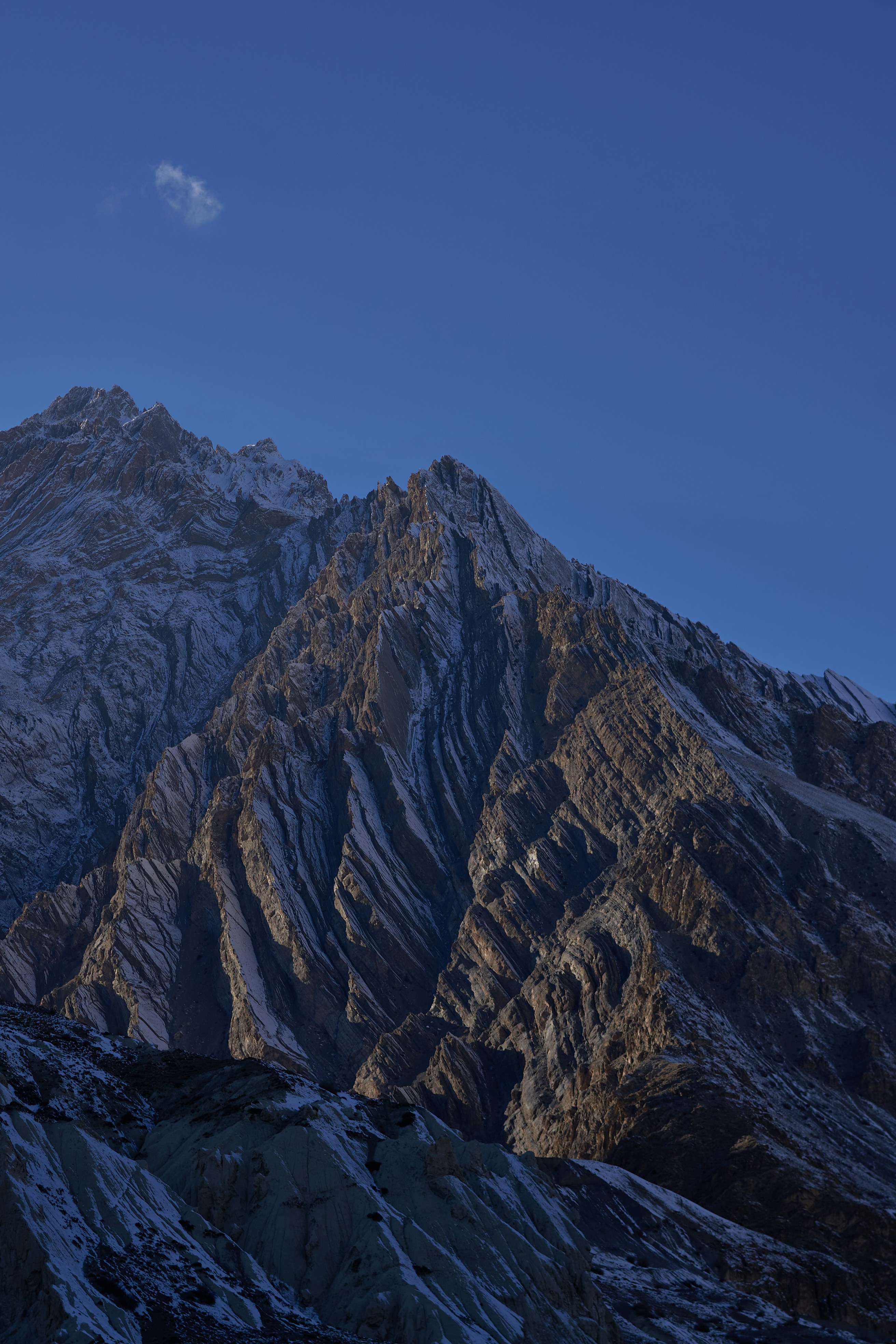 A jagged mountain peak with snow-dusted rock faces under a clear blue sky