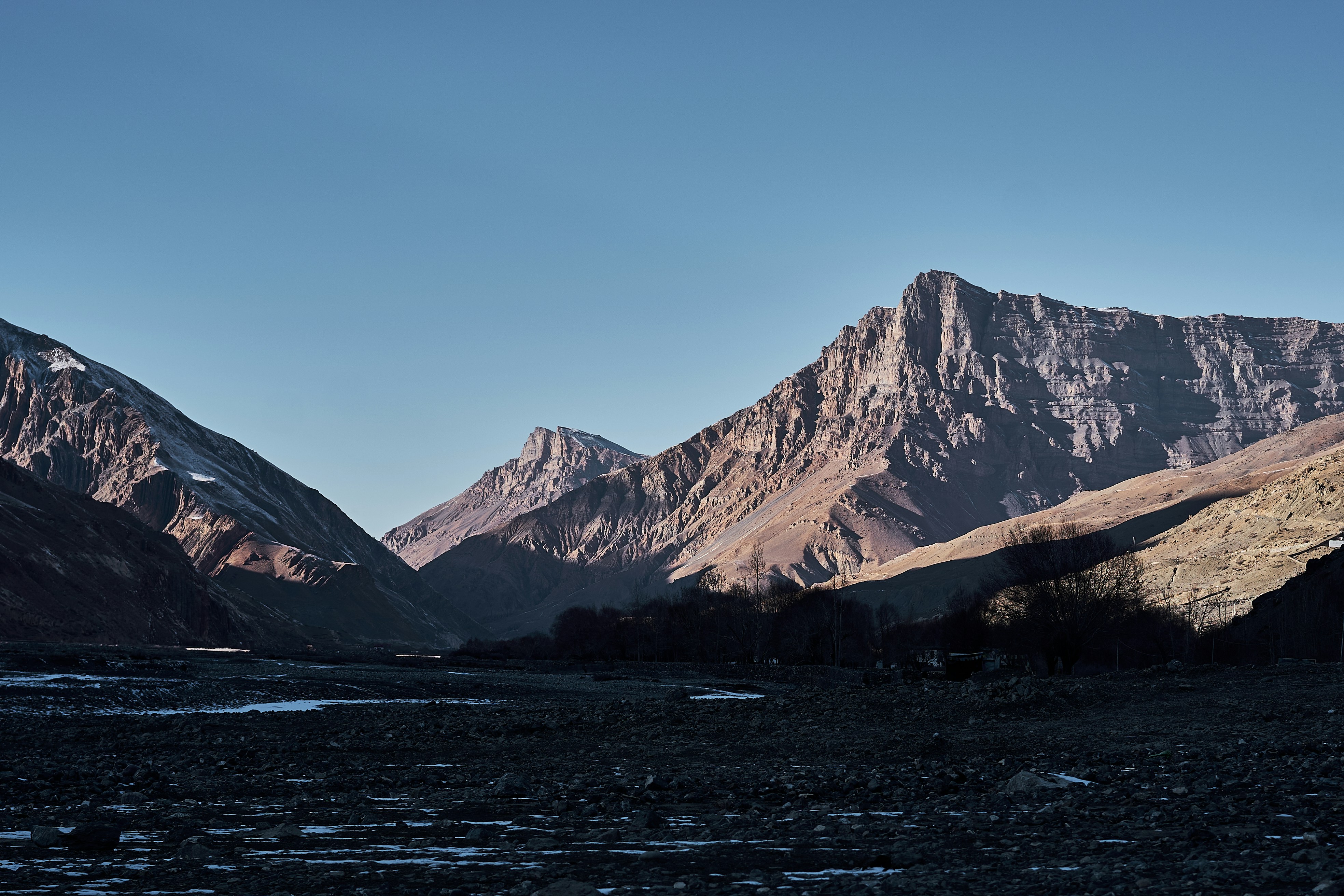 Rugged brown mountains rising above a dark rocky valley under a clear blue sky