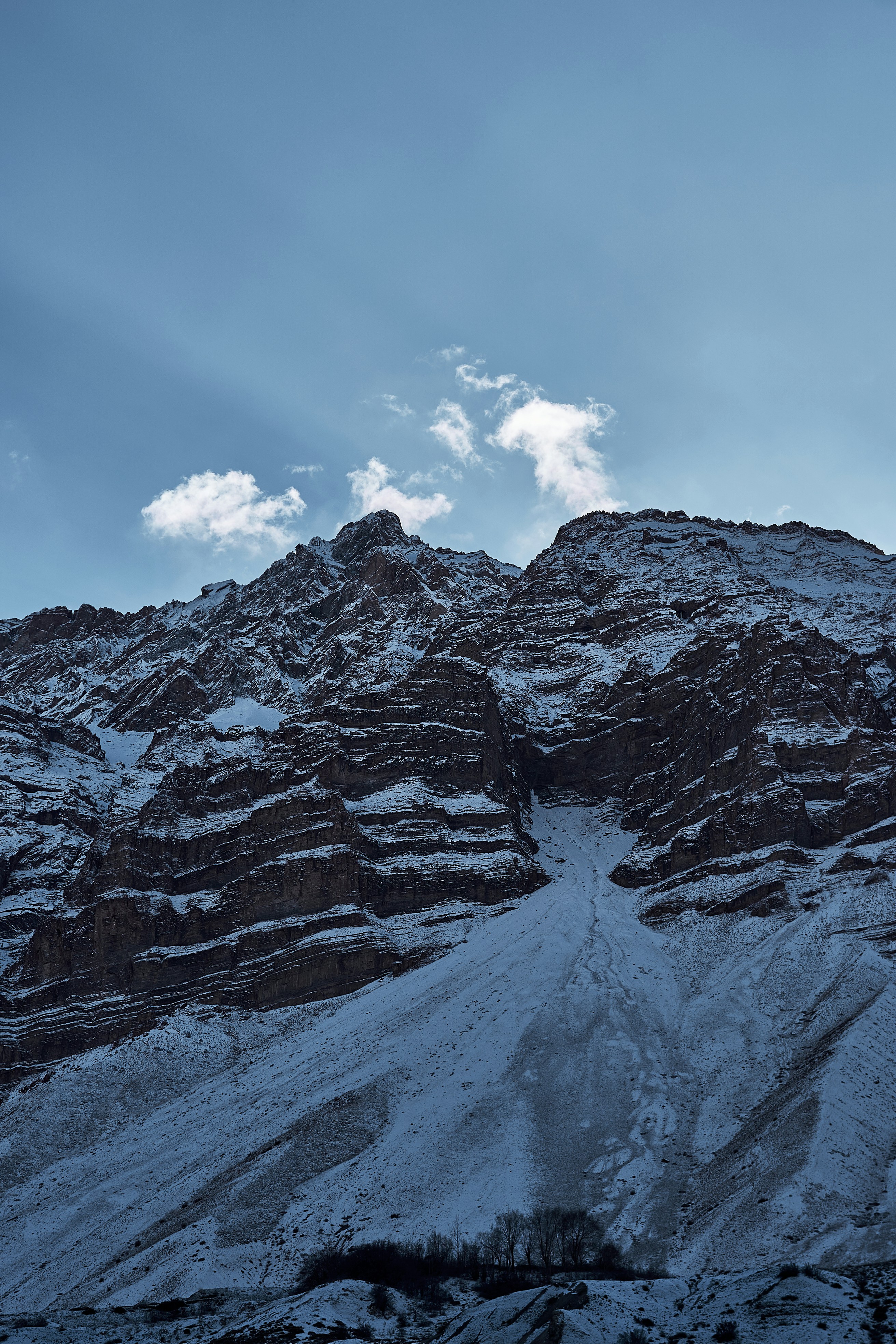 A rugged snow-covered mountain peak under a clear blue sky with light clouds