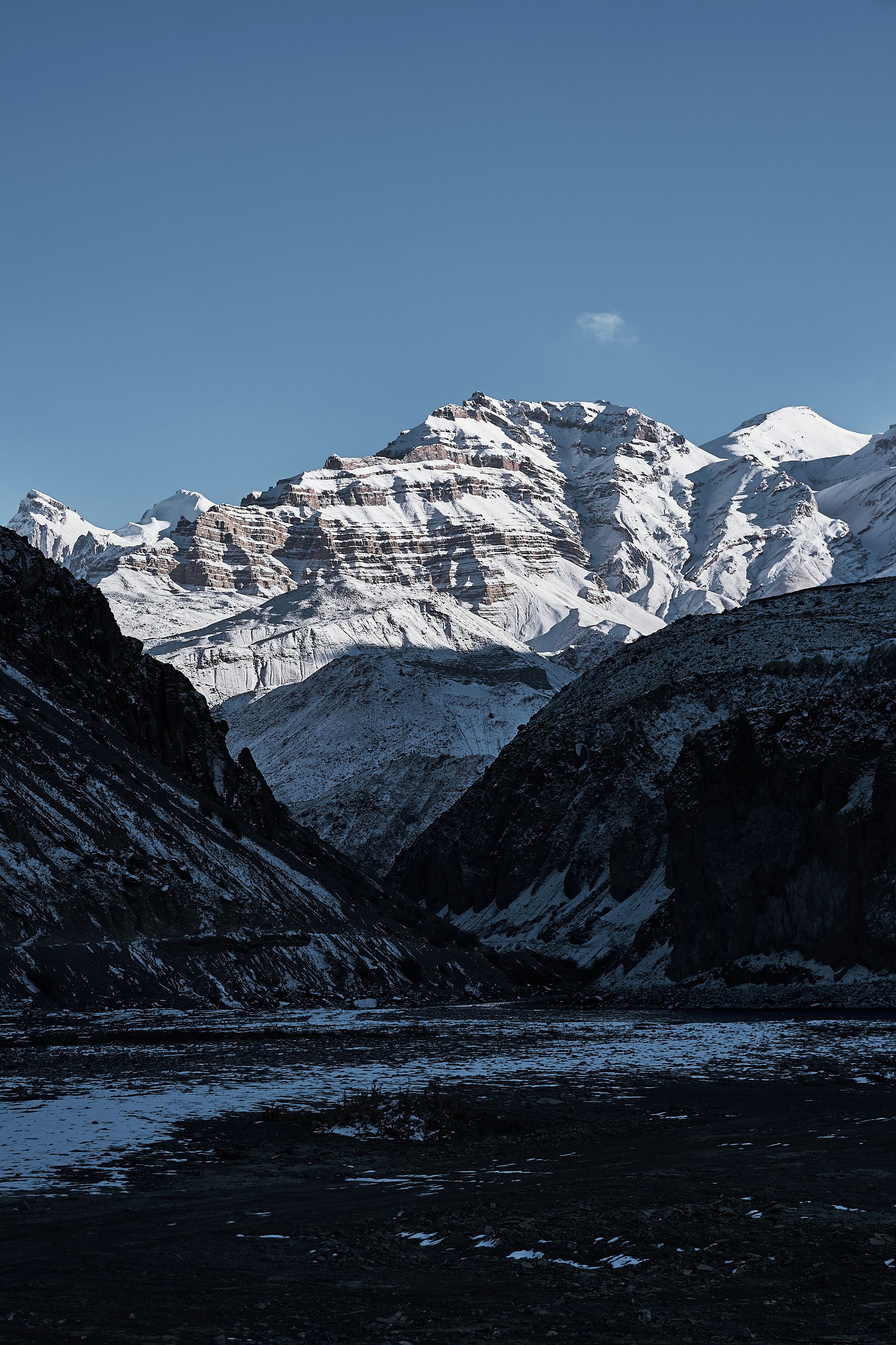 Snow-covered mountain peaks rising above a dark rocky valley under a clear sky