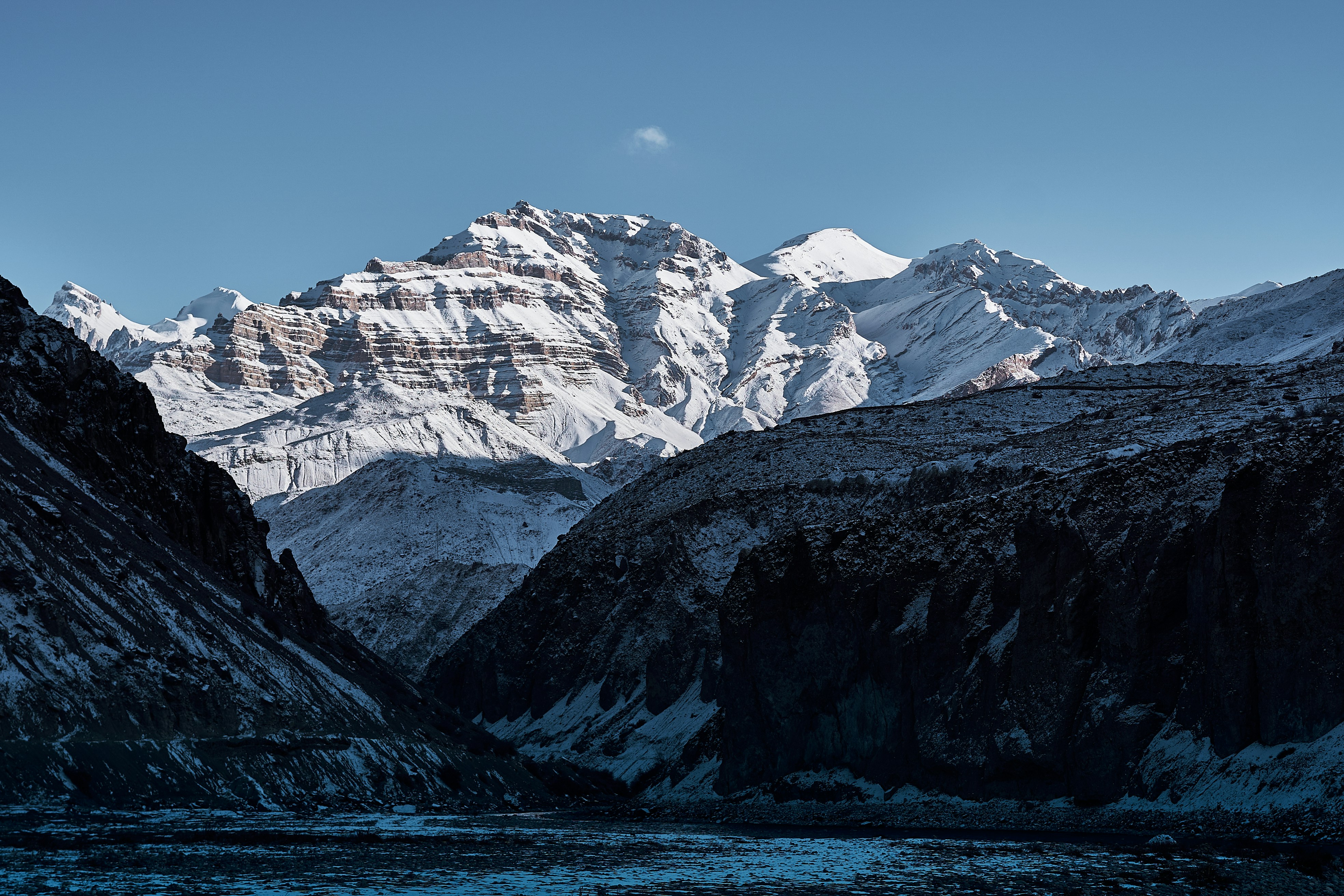 Snow-covered mountain peaks rising above a dark rocky valley under a clear sky