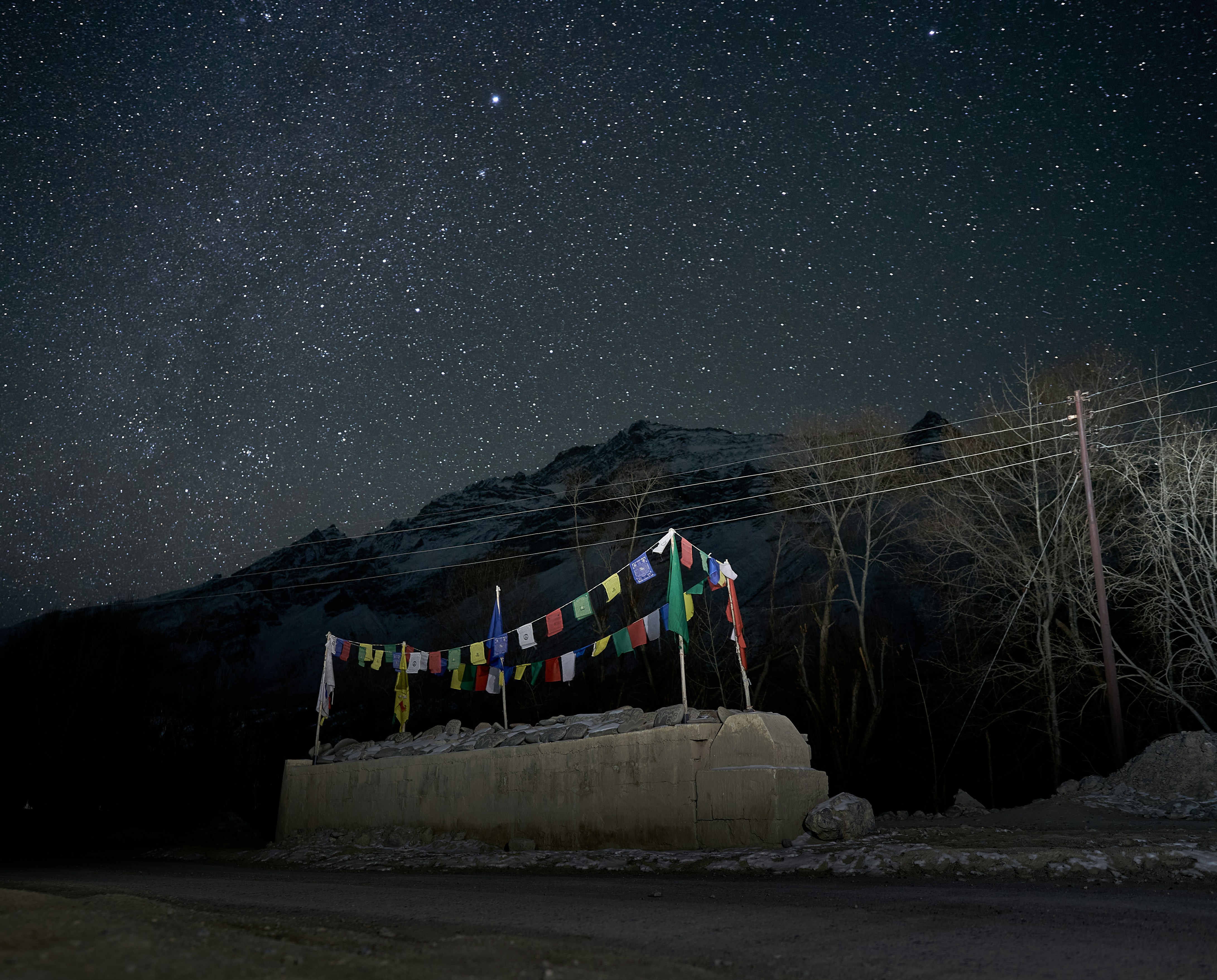 Colorful prayer flags strung above a stone wall beneath a starry night sky