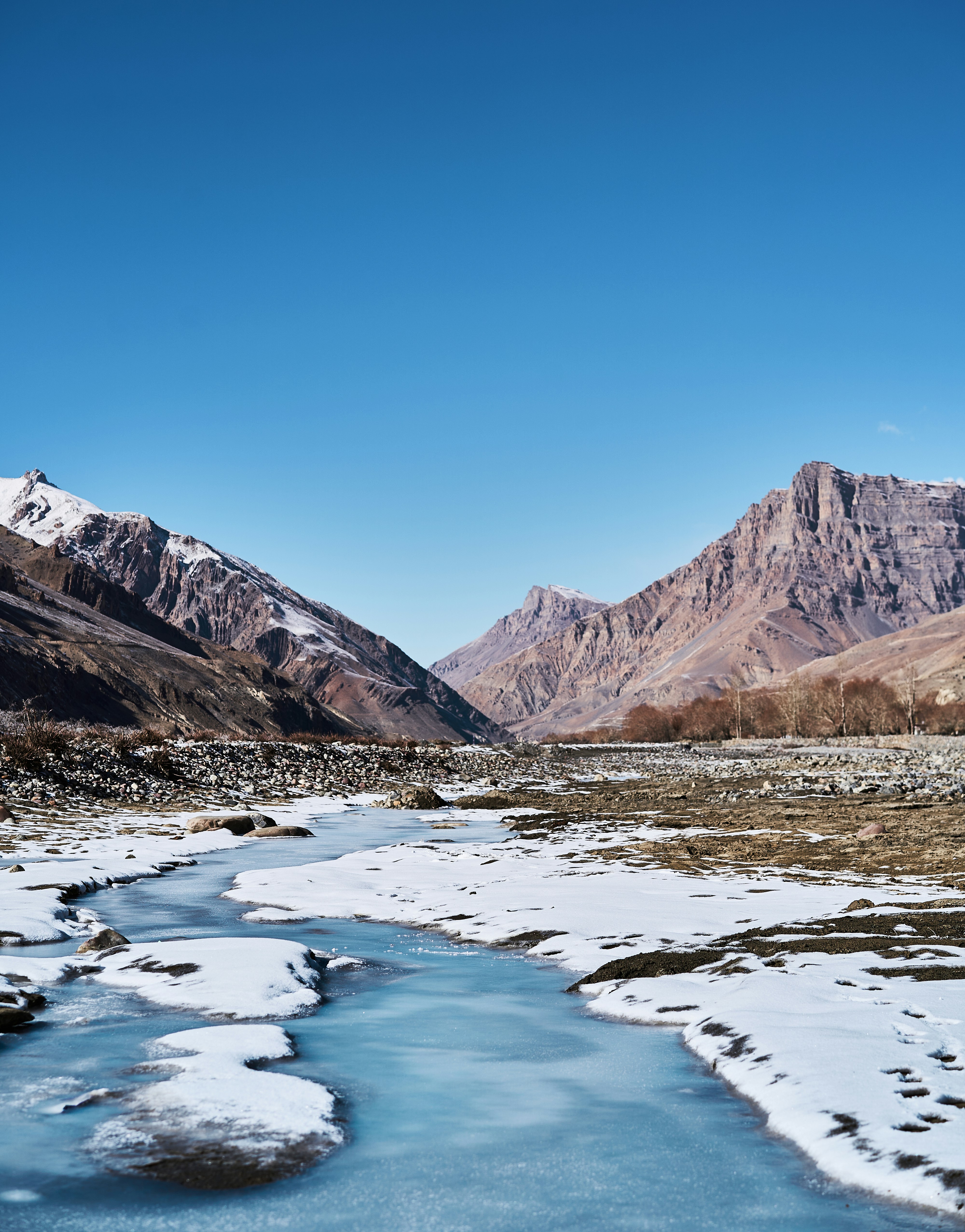 A frozen stream winding through a valley between high rocky mountains under clear sky