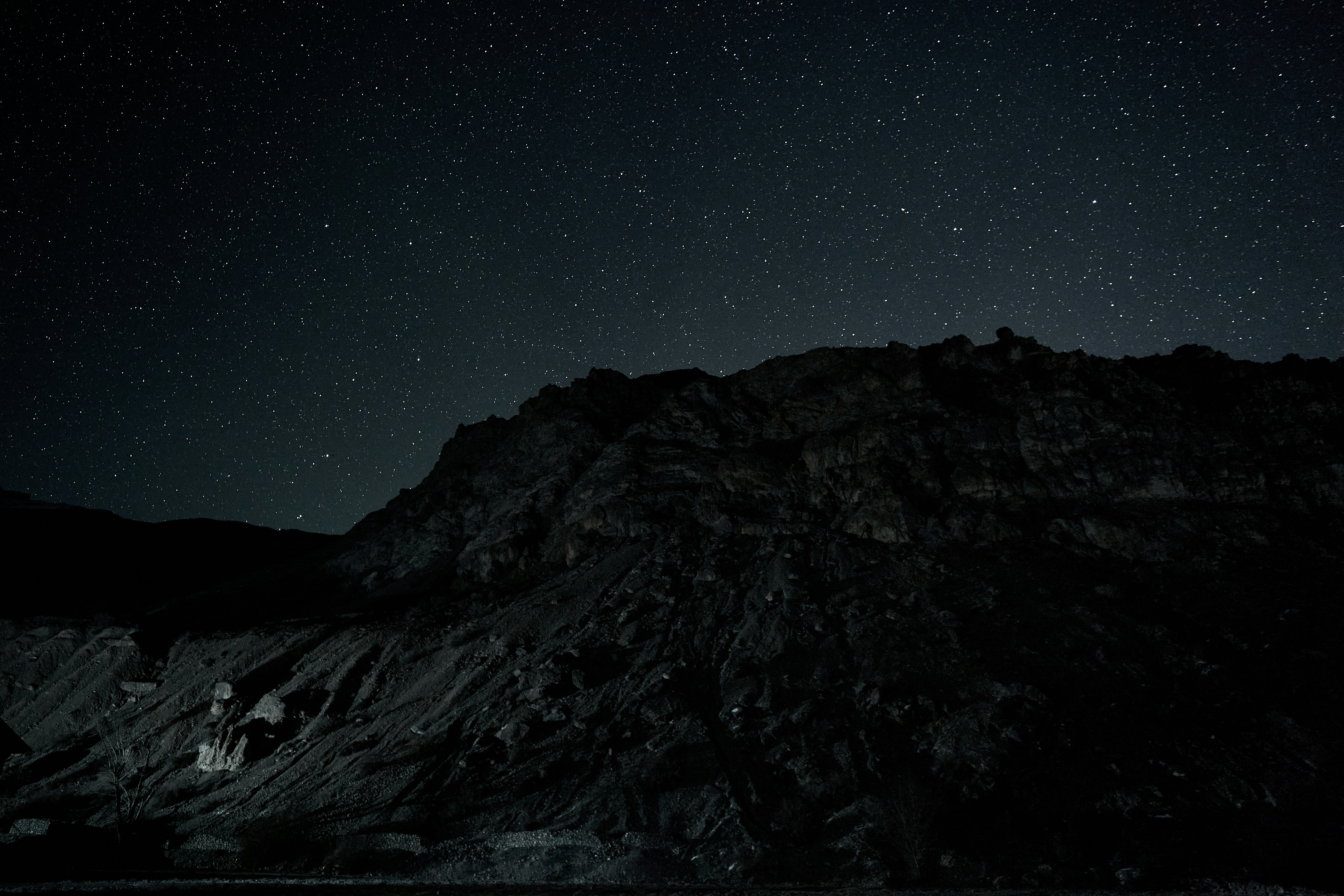 A dark rocky mountain silhouette against a vast night sky filled with stars