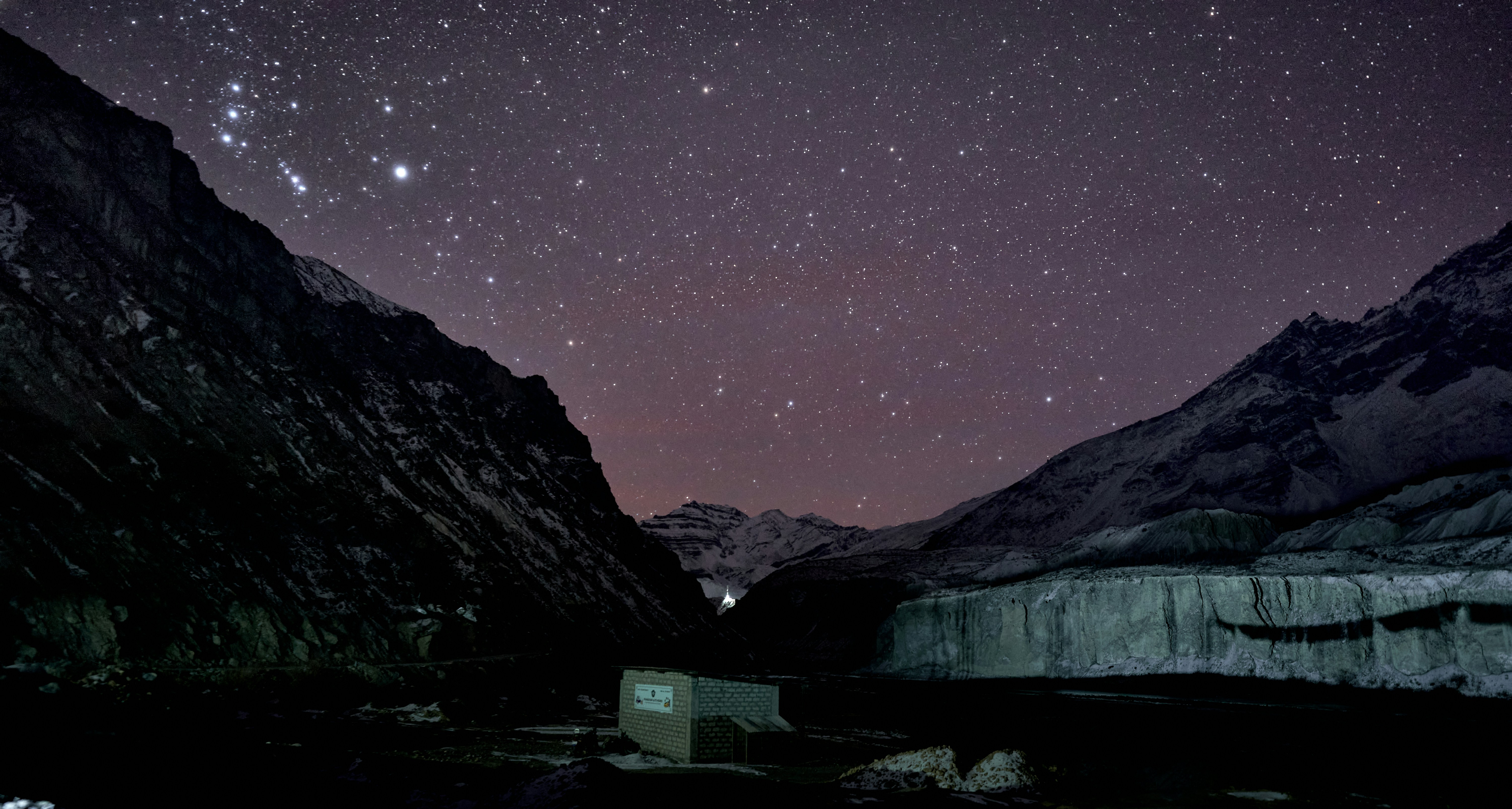 A small building in a dark valley beneath a vast starry night sky