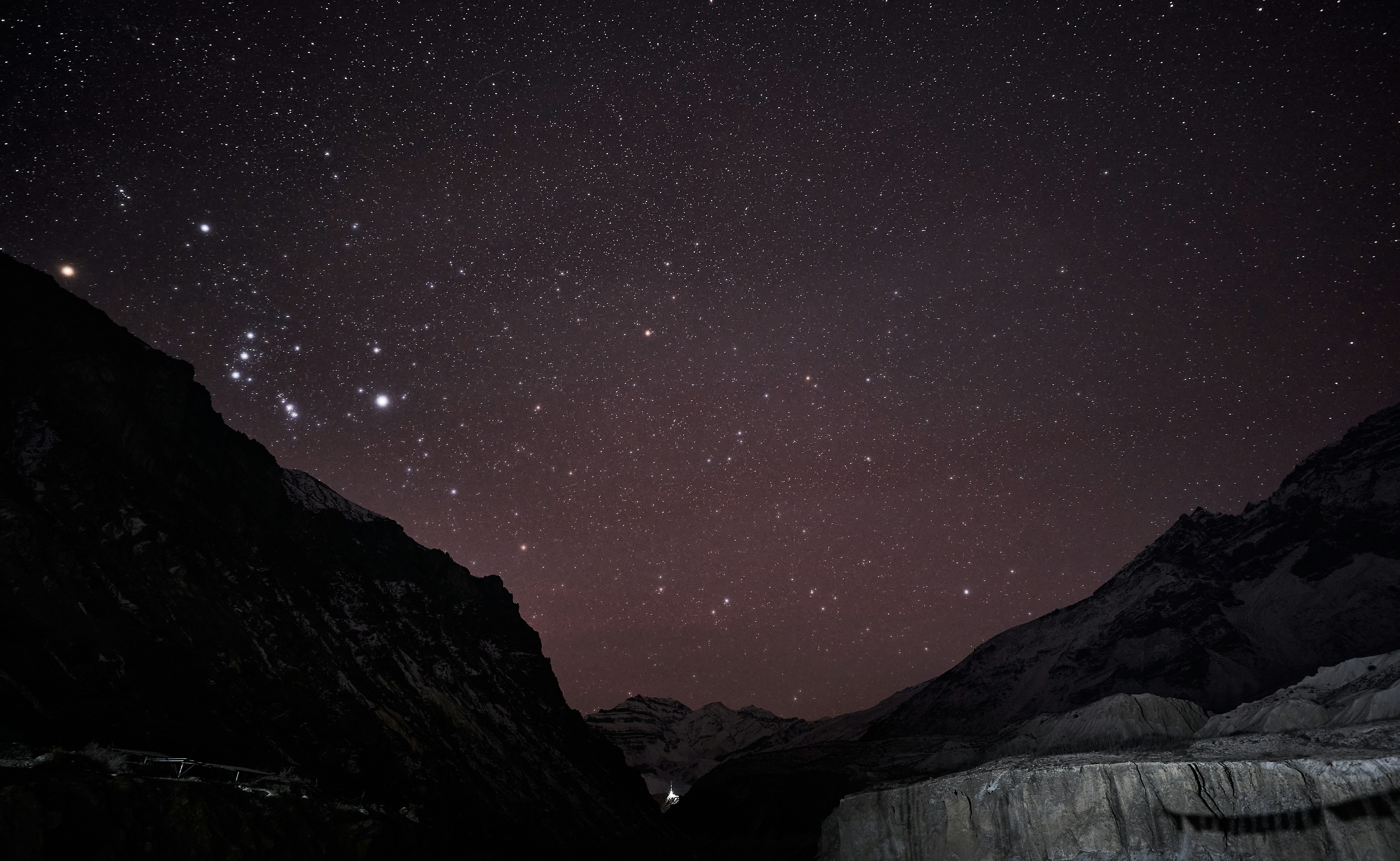 A starry night sky above dark mountain silhouettes and a deep valley