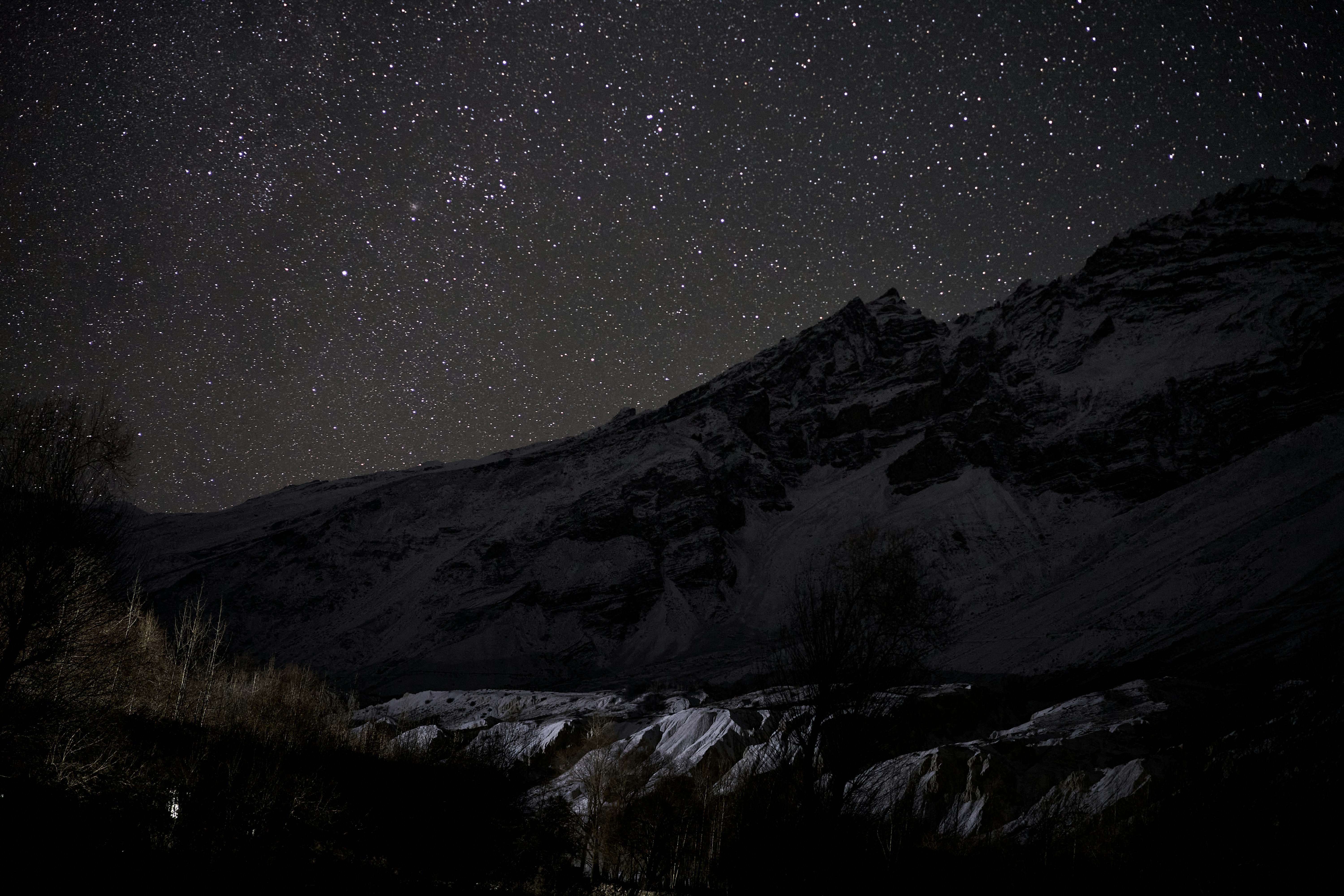 A starry night sky above a dark, snow-covered mountain range
