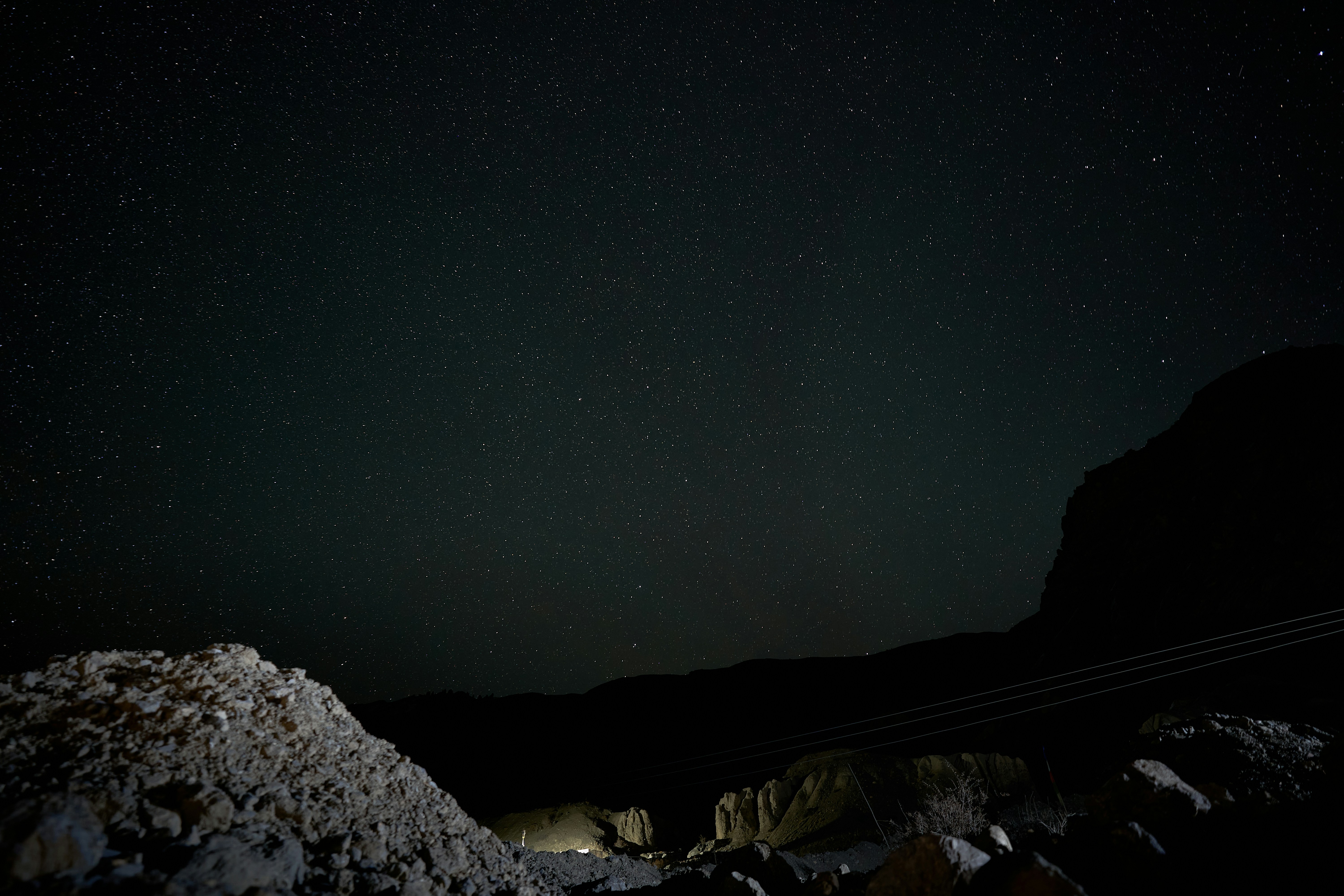 A starry night sky above a dark rocky landscape with power lines