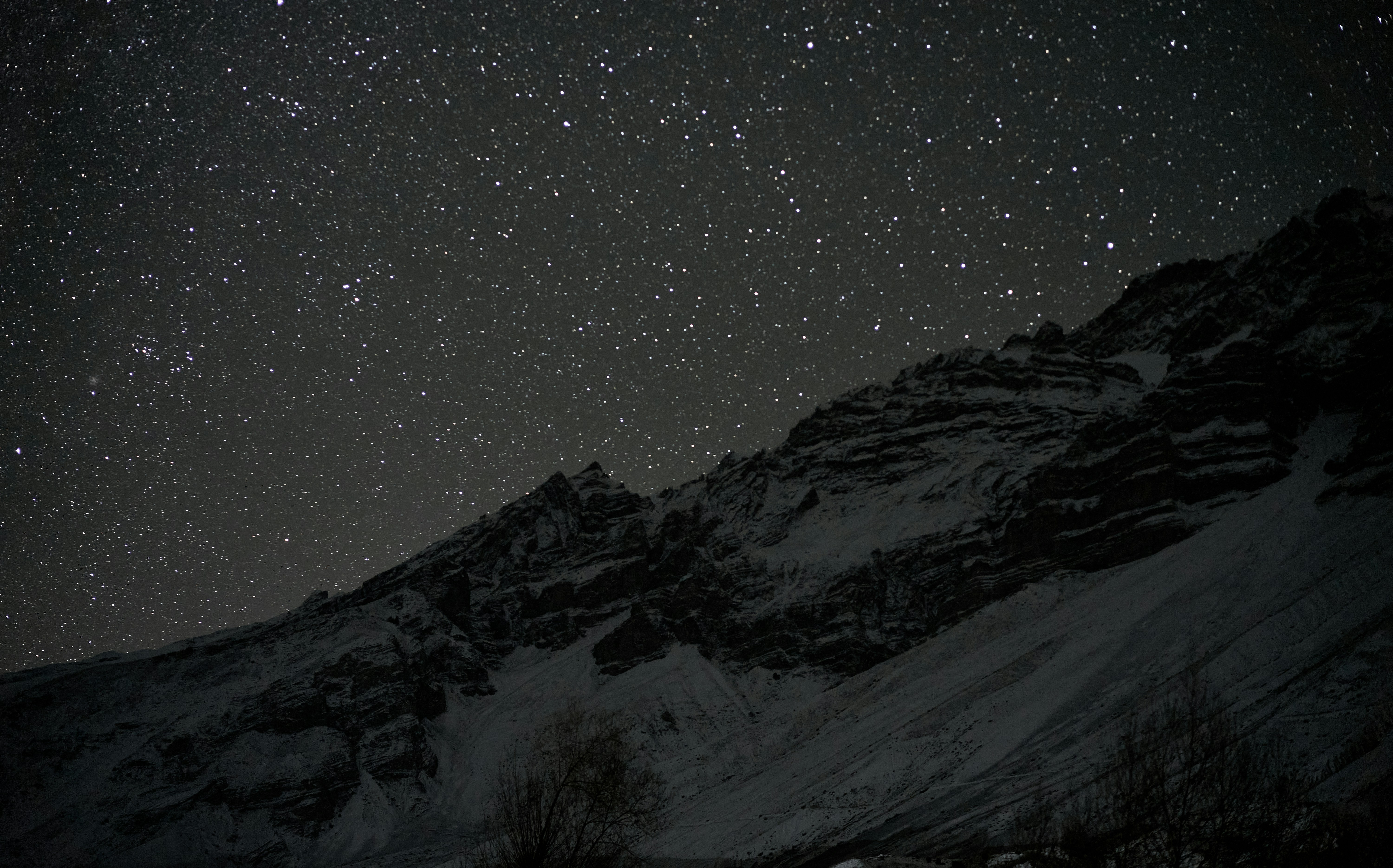 A starry night sky above a dark, snow-covered mountain ridge