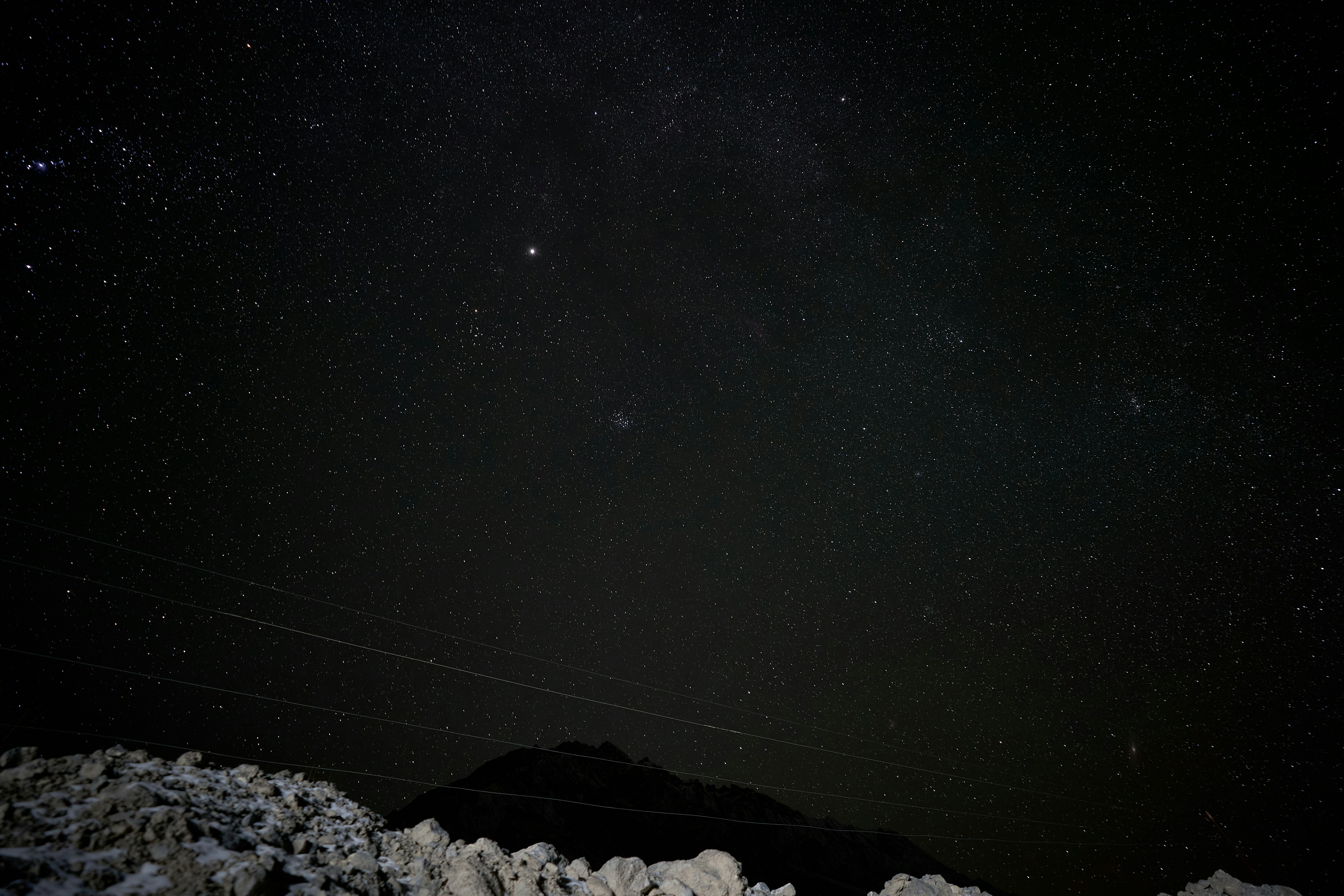 A dark night sky filled with stars above a rocky mountain silhouette
