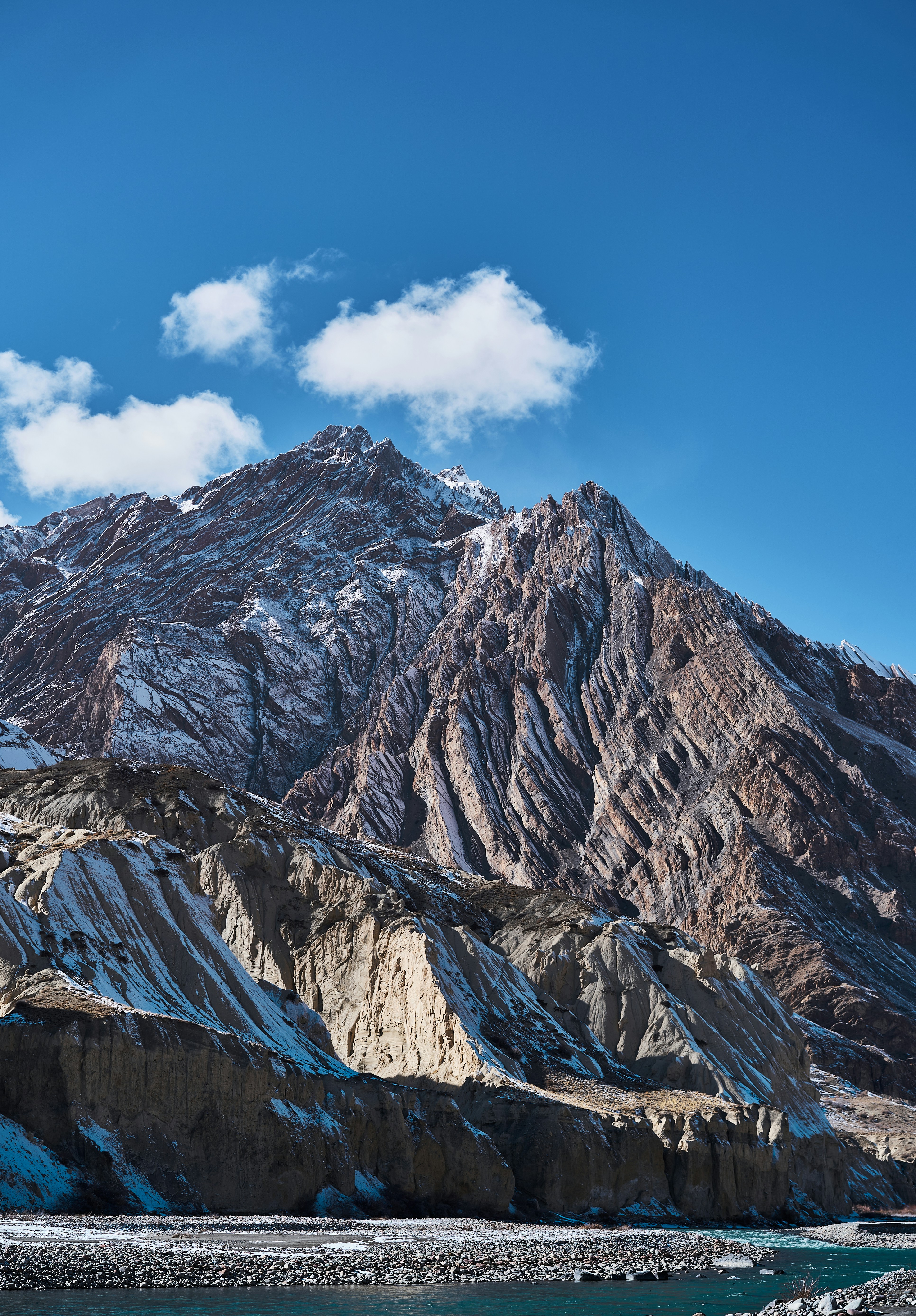 Snow-dusted jagged mountain peaks above a river under a clear blue sky