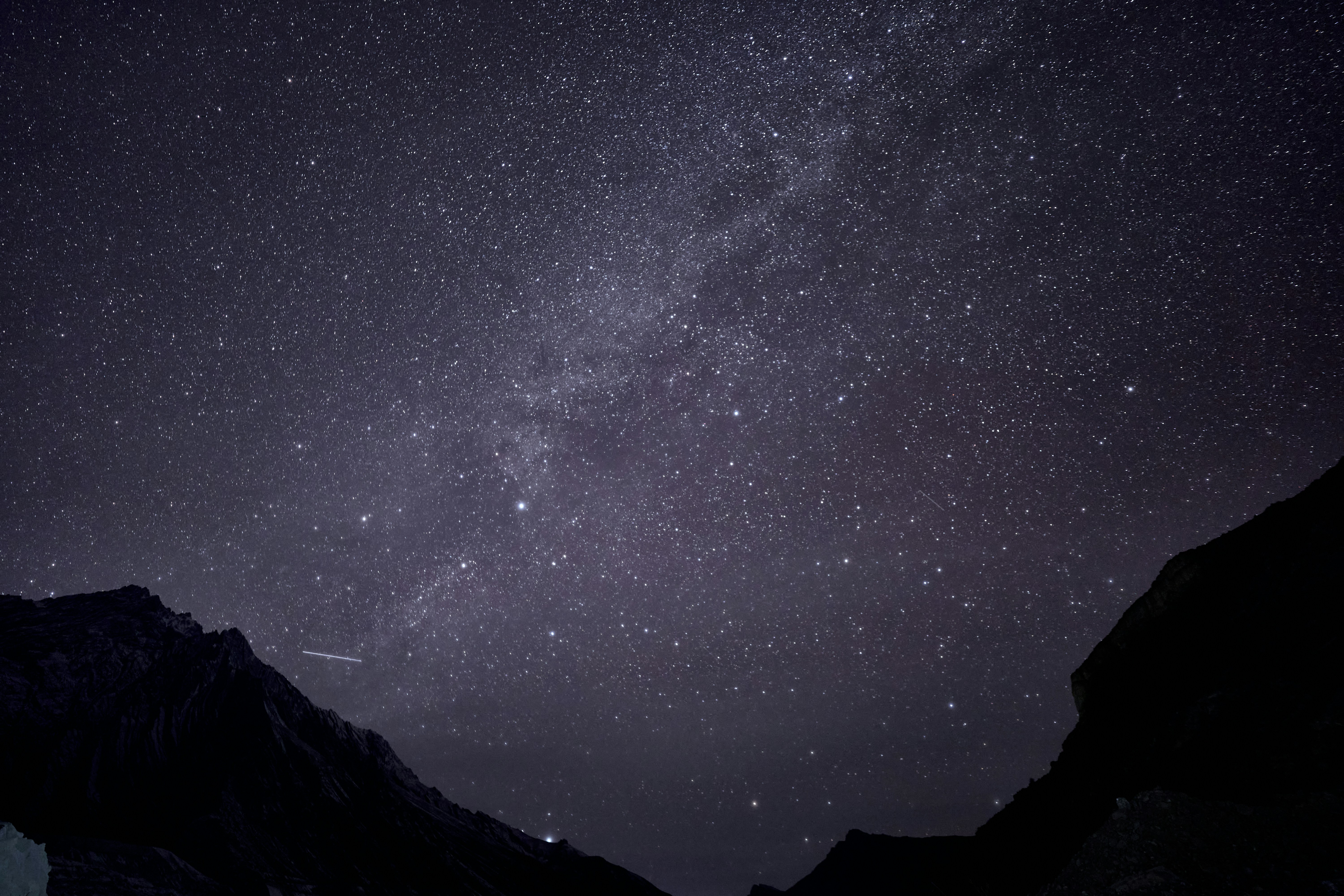 A vast starry night sky above the dark silhouettes of jagged mountain peaks