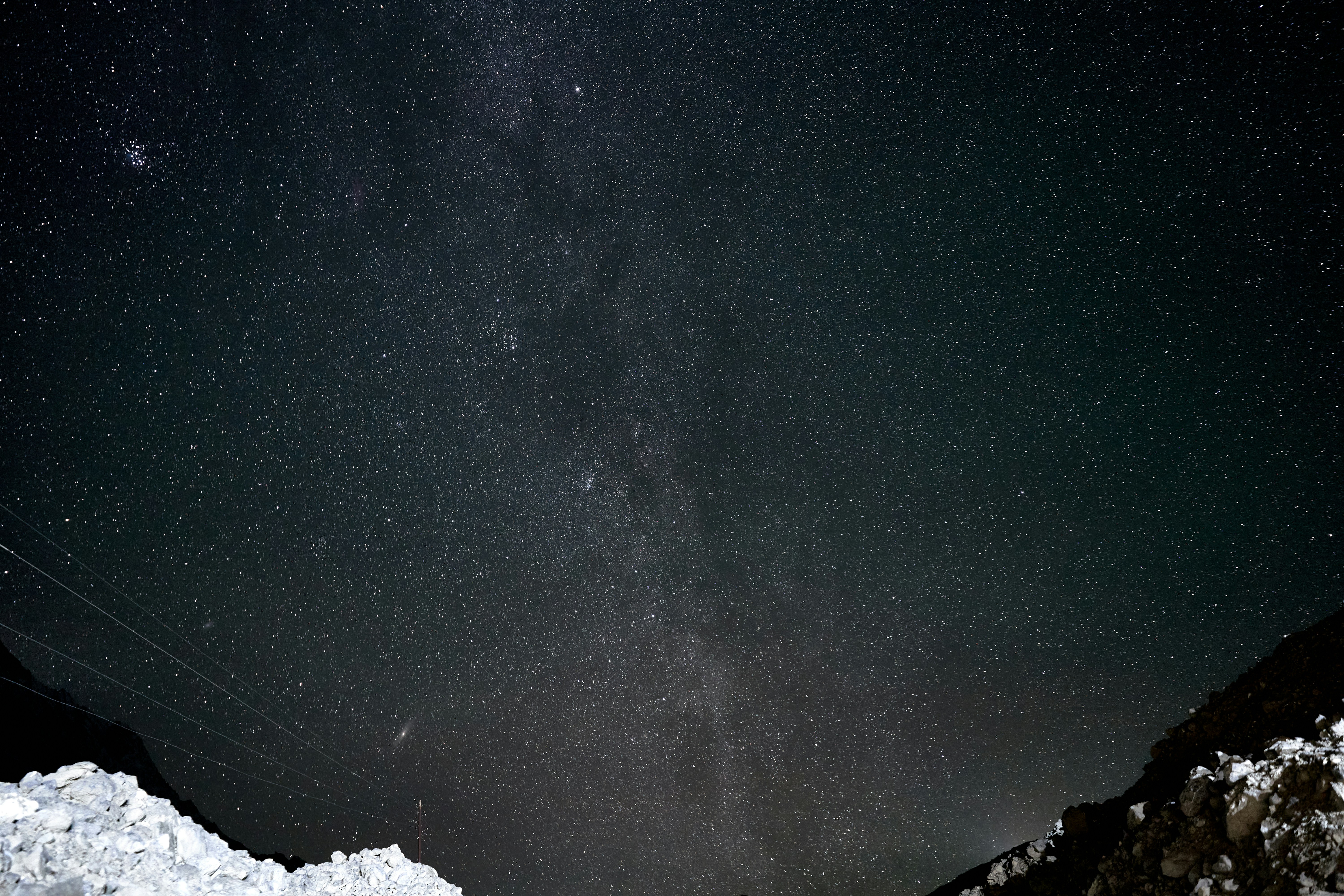 A vast starry night sky above a dark rocky mountain landscape