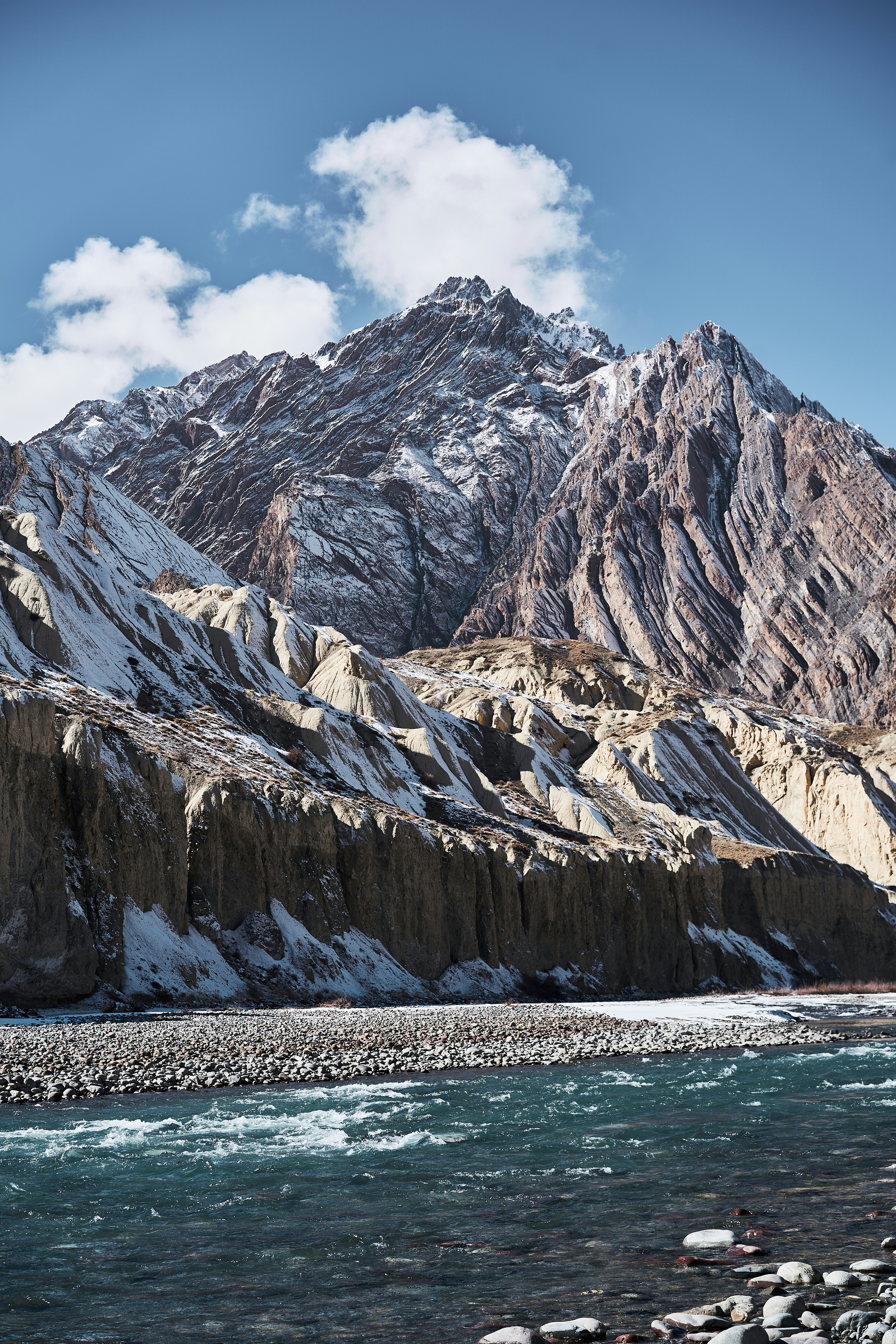 A turquoise river flowing past snow-dusted rocky cliffs and high mountain peaks
