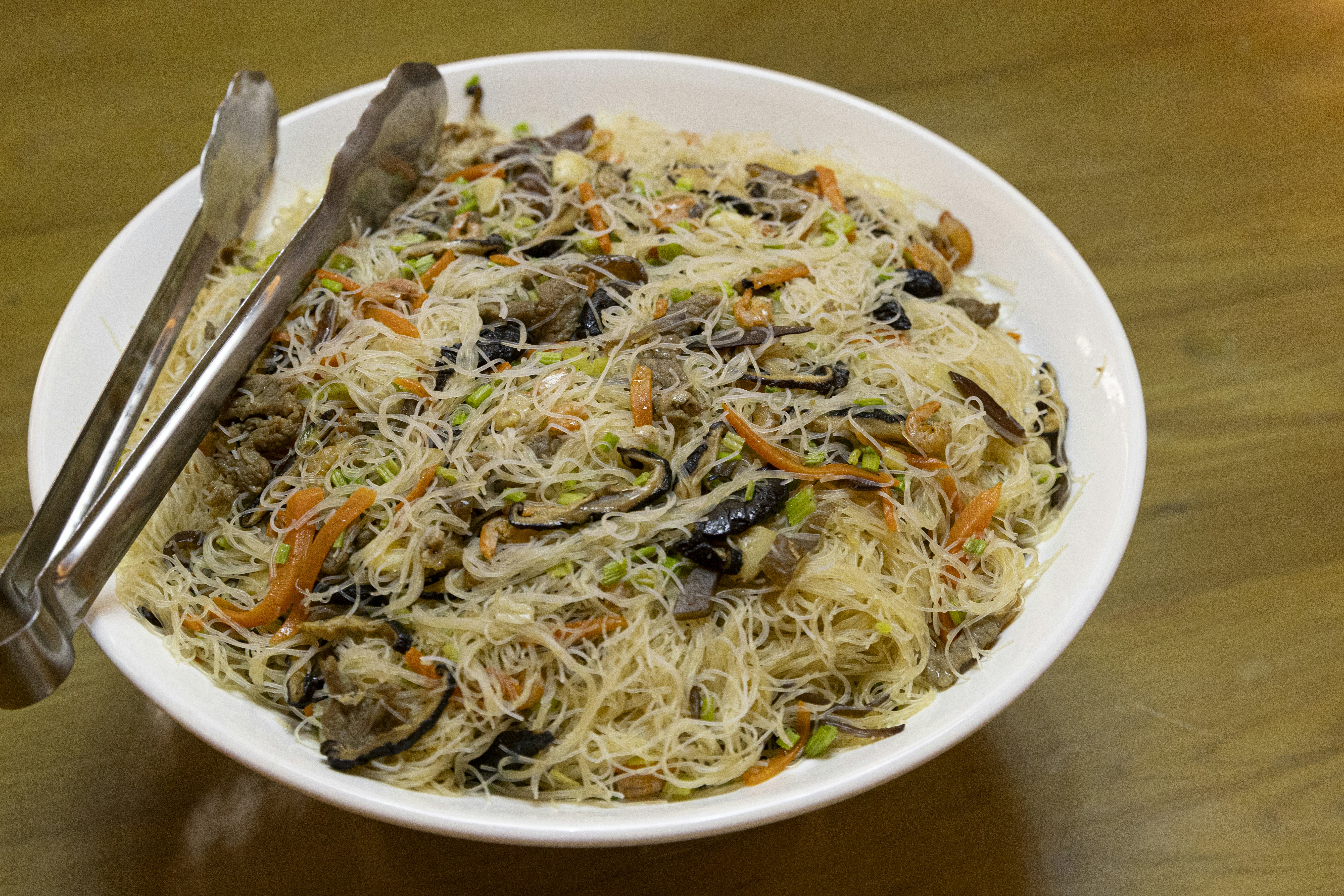 A large white bowl of stir-fried rice vermicelli noodles with vegetables and meat