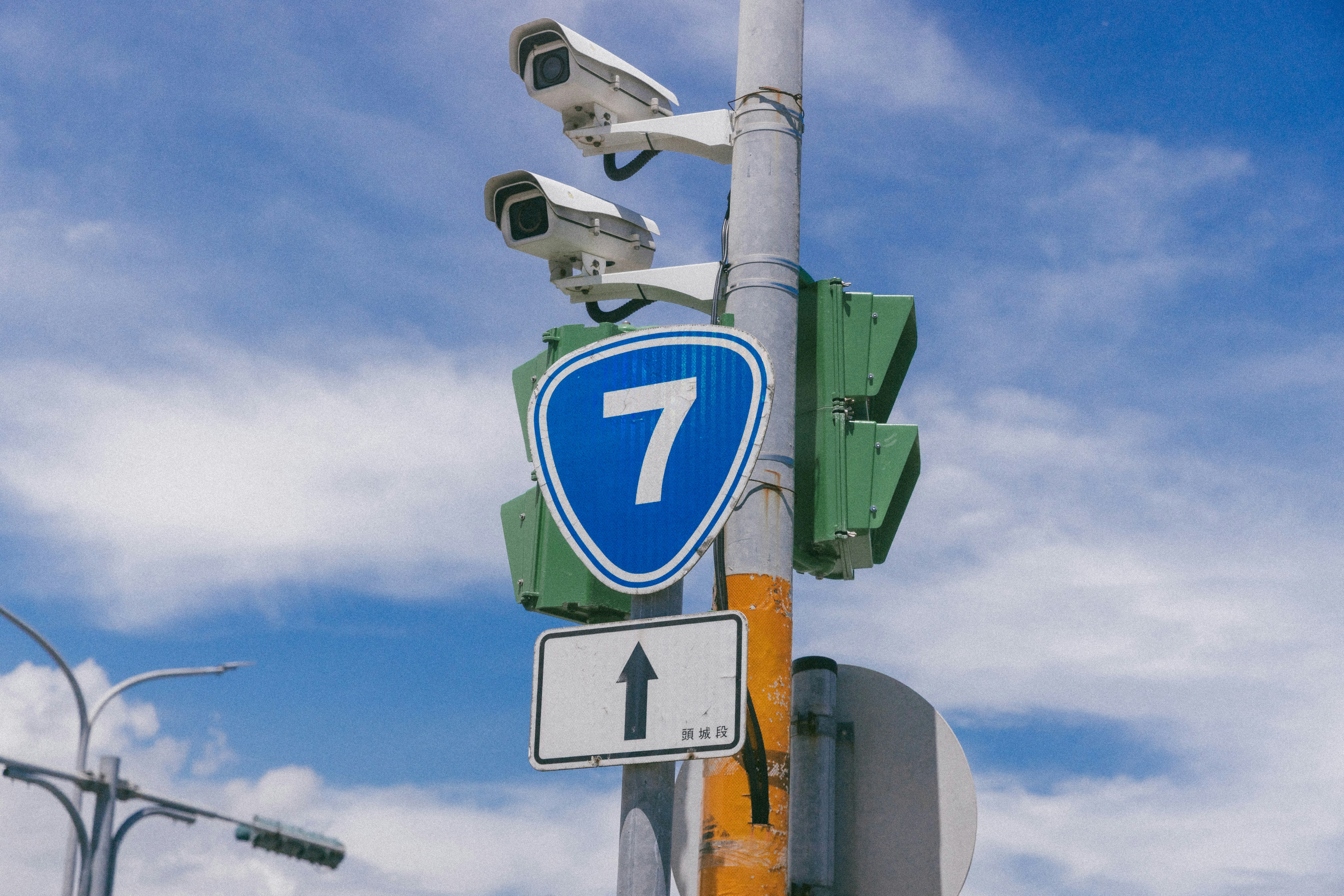 Two security cameras mounted on a pole above a blue number seven sign