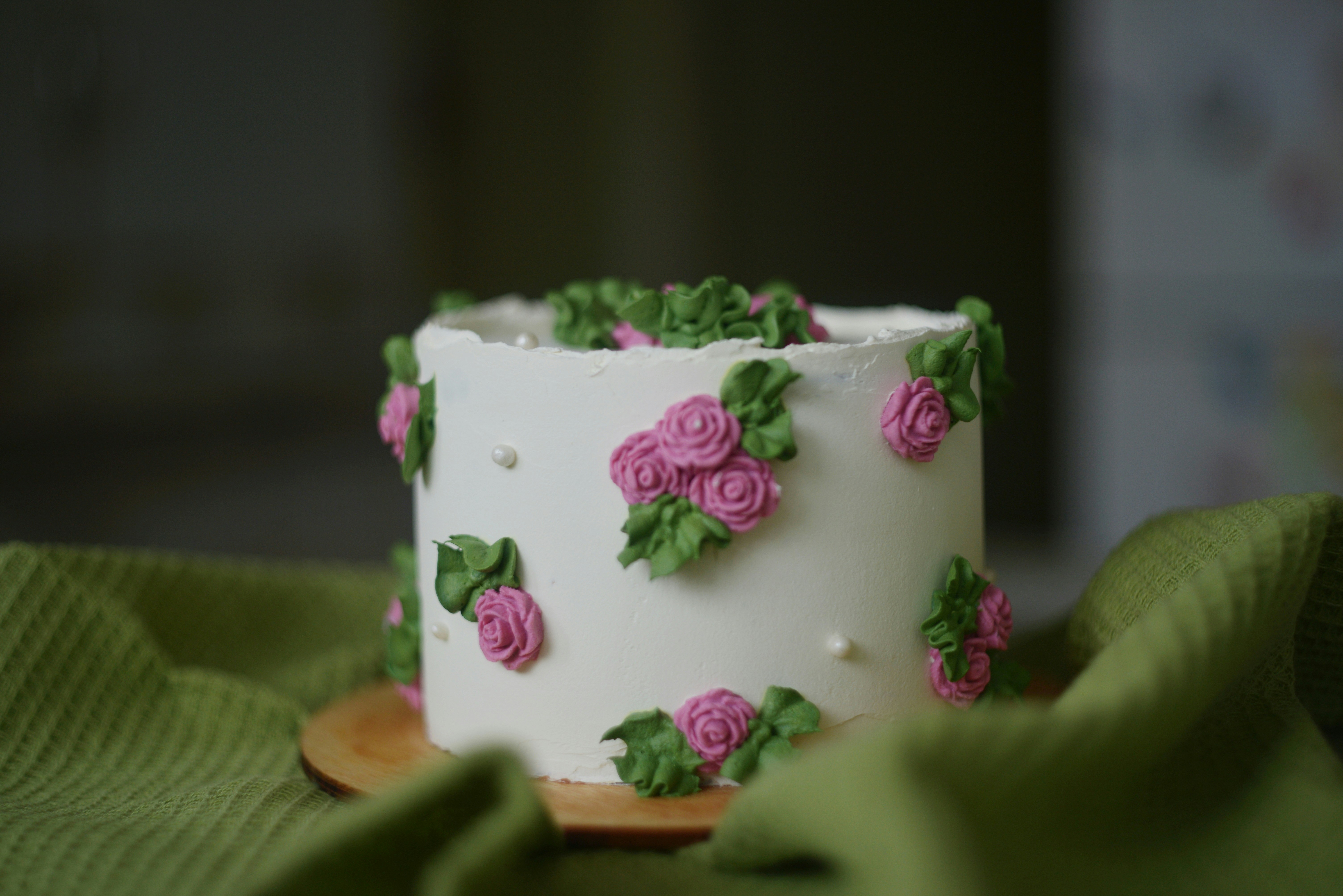 A white cake decorated with pink frosting roses and green leaves on a green cloth