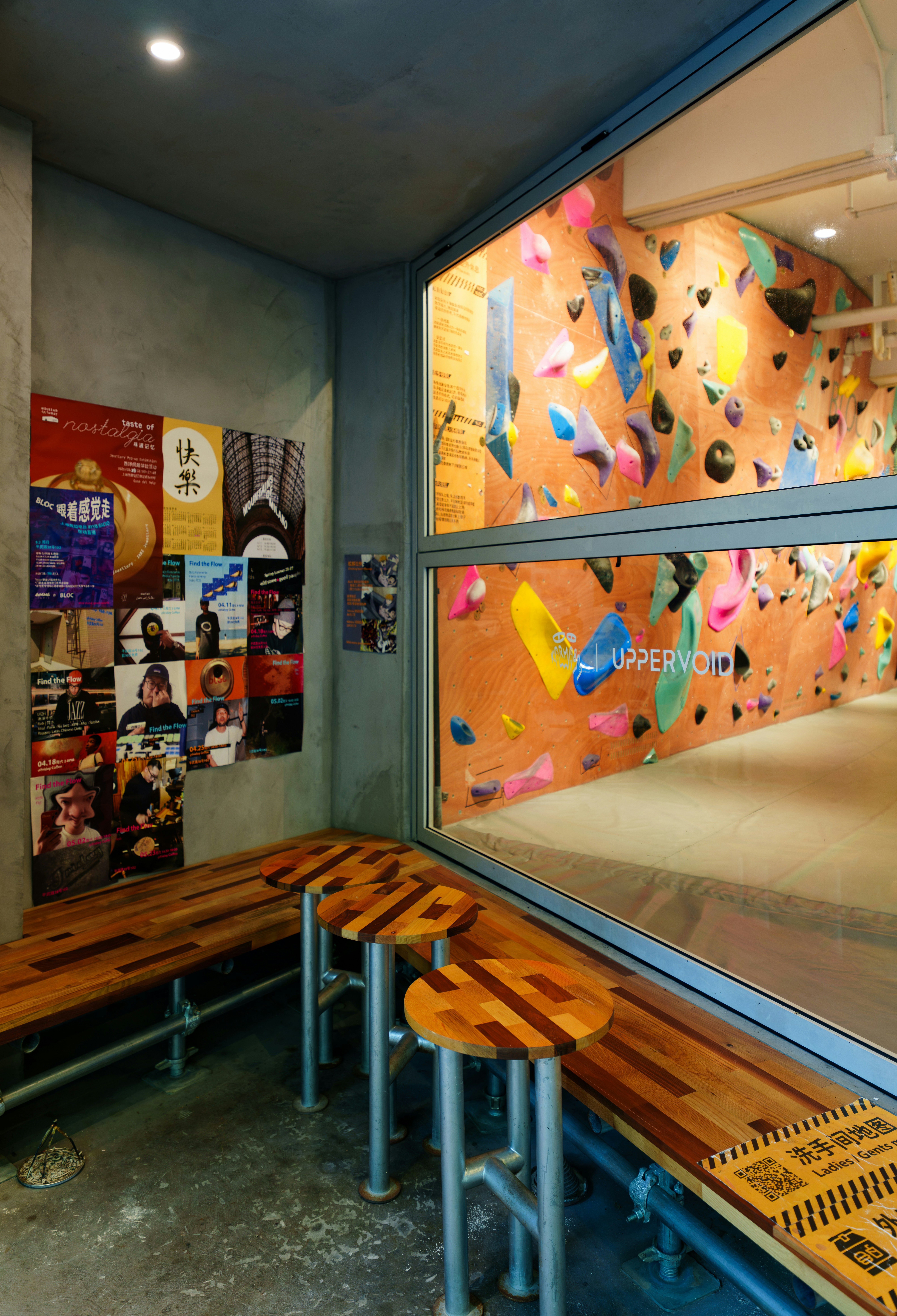Three wooden stools and a bench beside a climbing wall with colorful holds