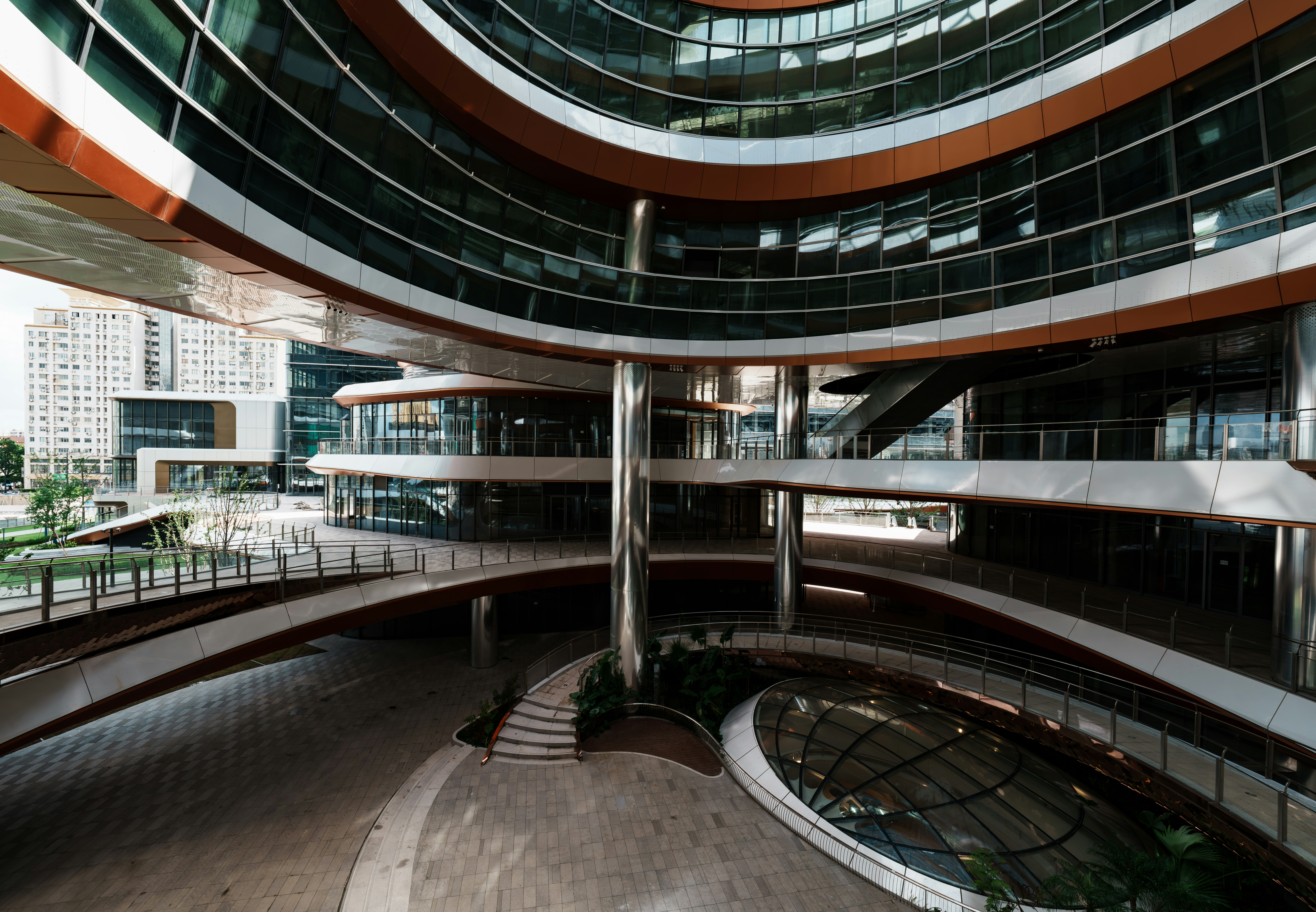 A modern circular building with glass windows and metallic pillars in an open courtyard