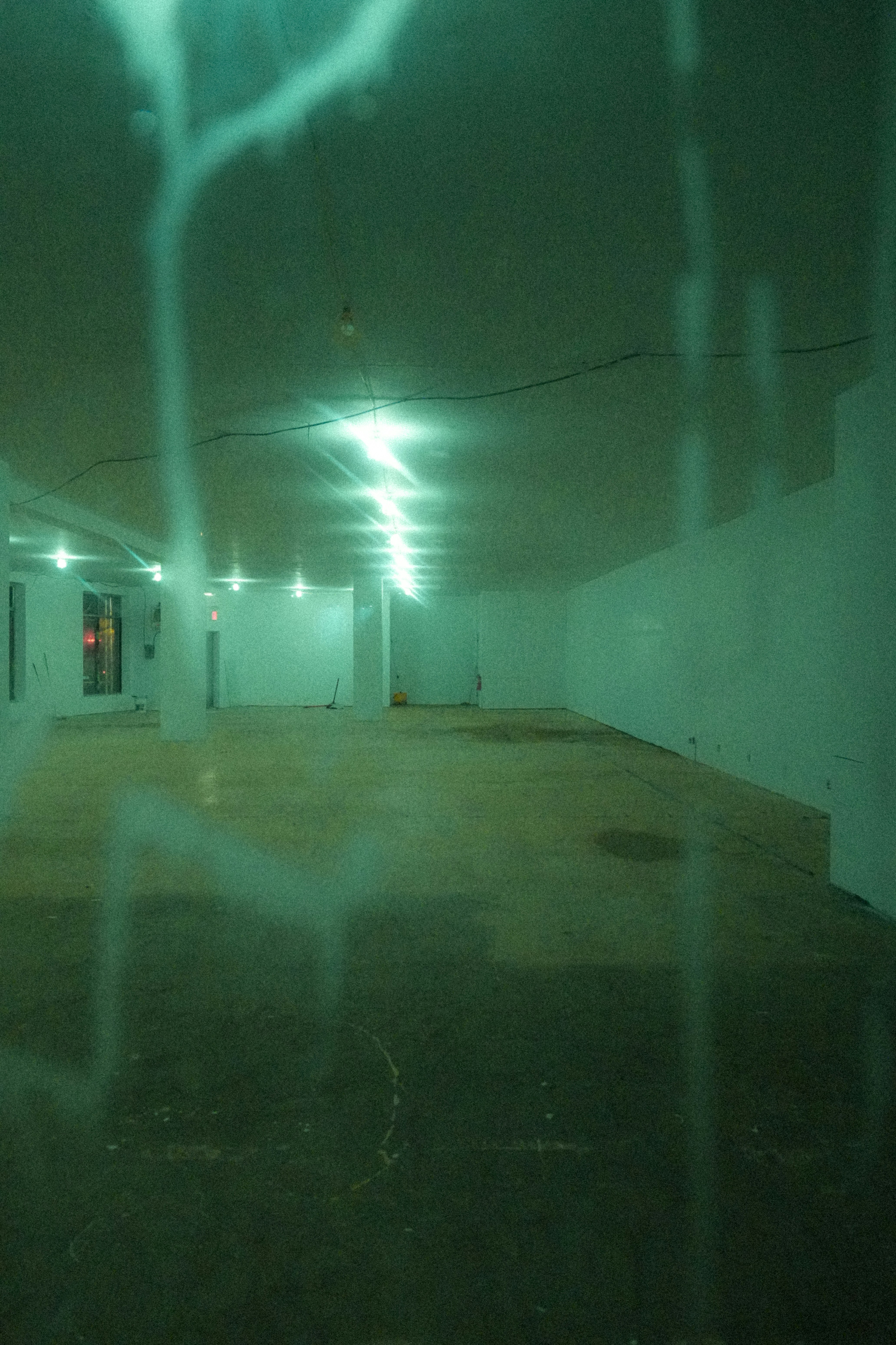 An empty commercial space with white walls and green overhead lighting