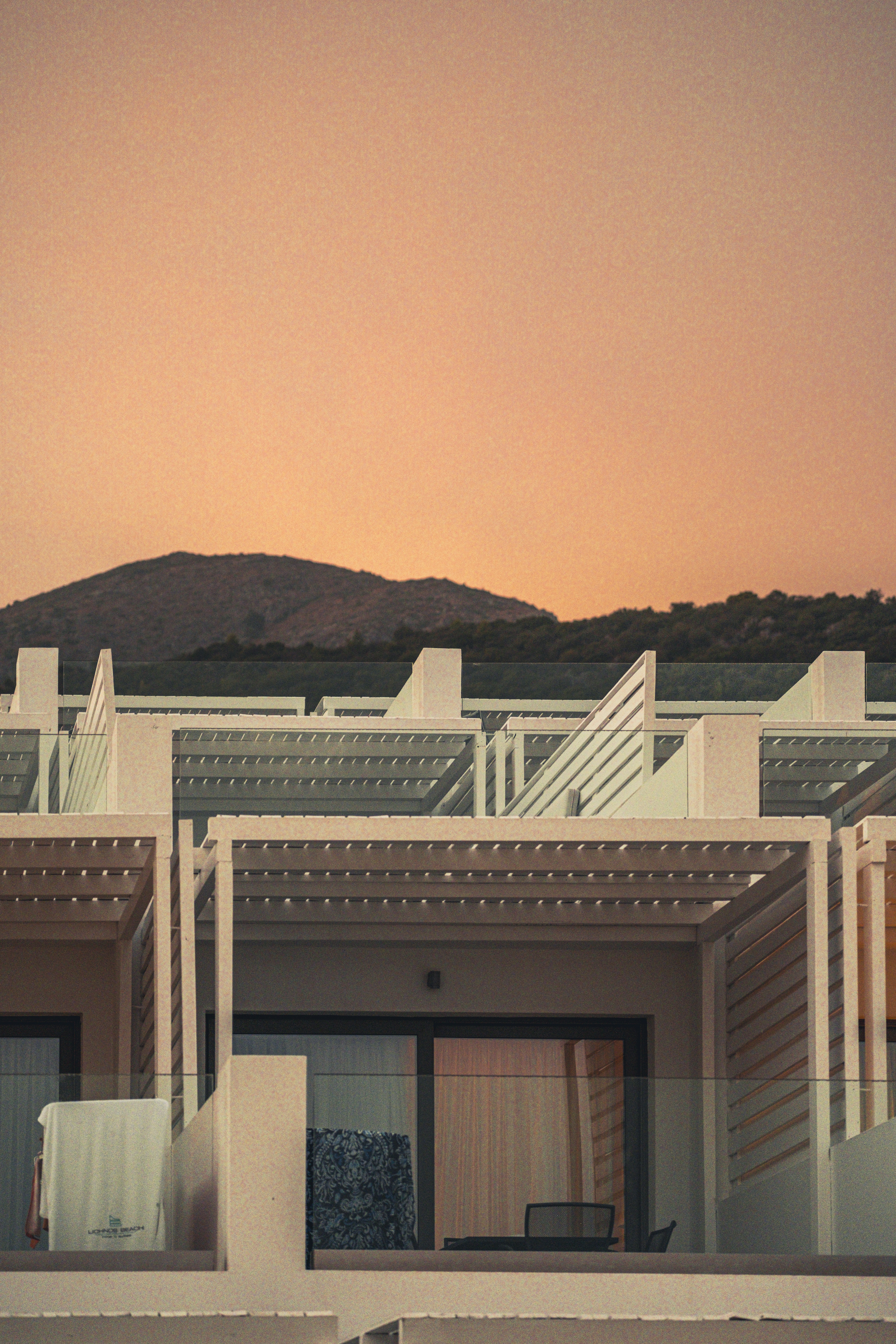 Modern hotel balconies with wooden pergolas against a warm orange sky and hills