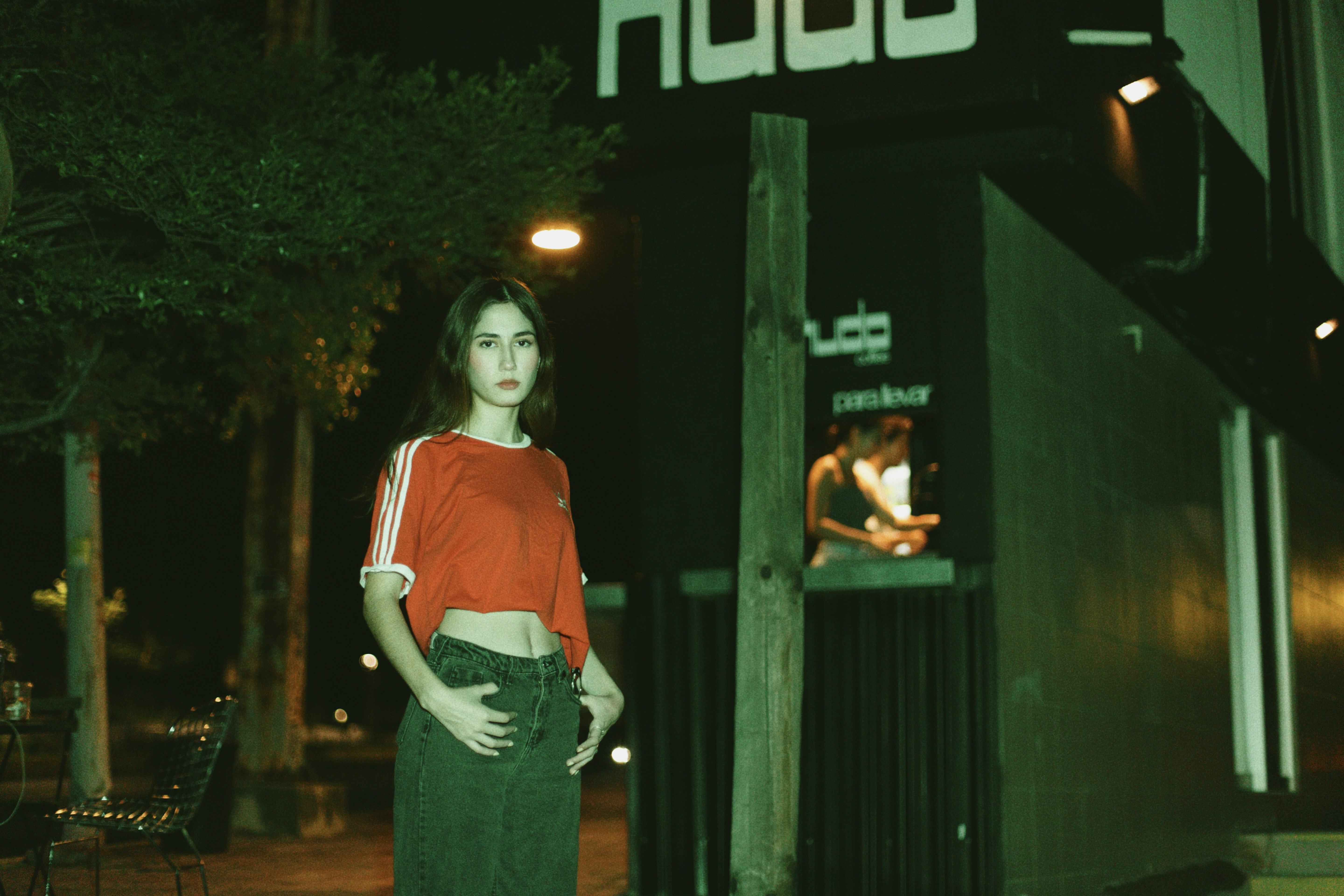A woman in a red crop top and jeans standing on a street at night