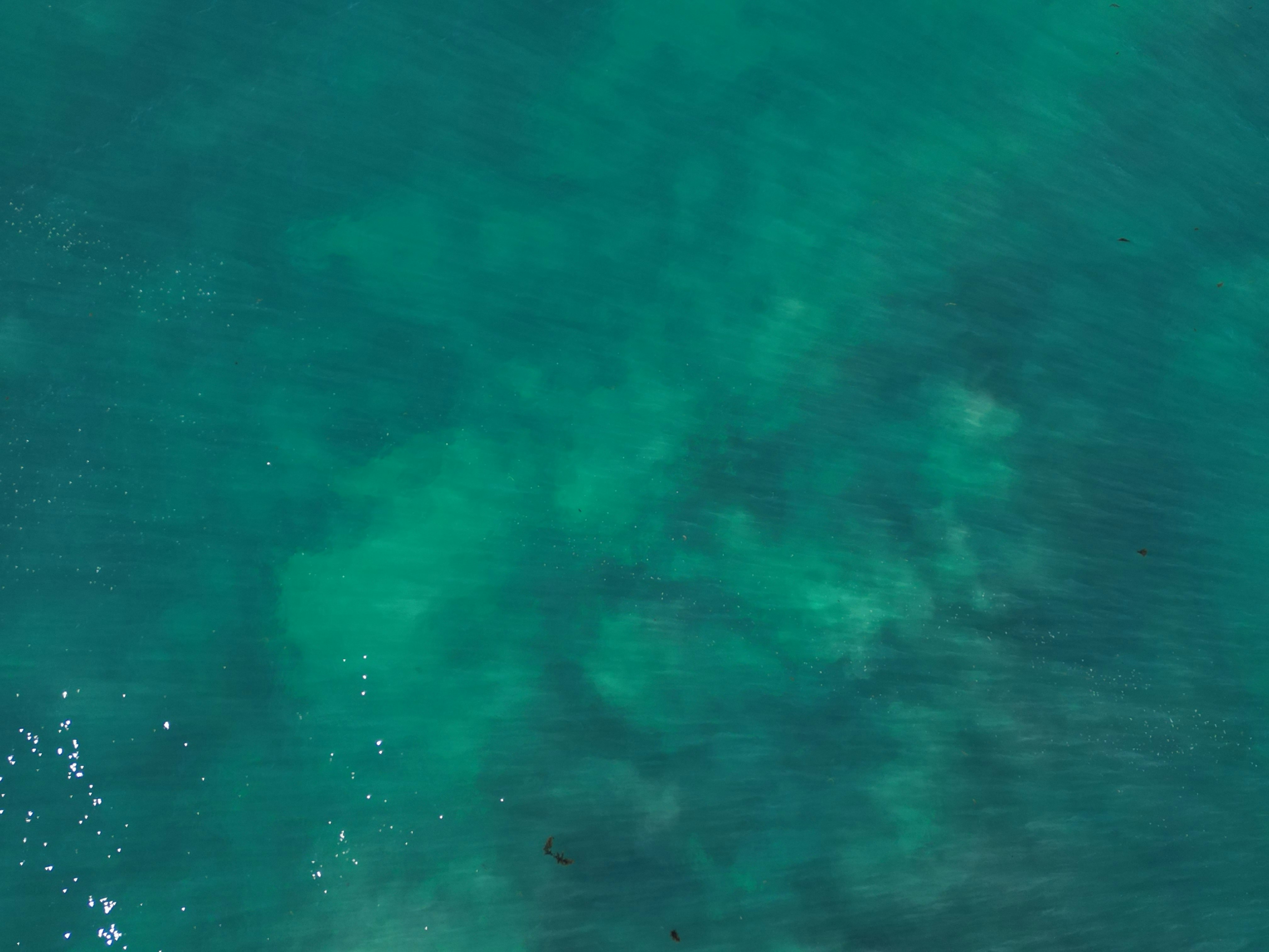 Aerial view of turquoise ocean water with sunlight reflecting on the surface