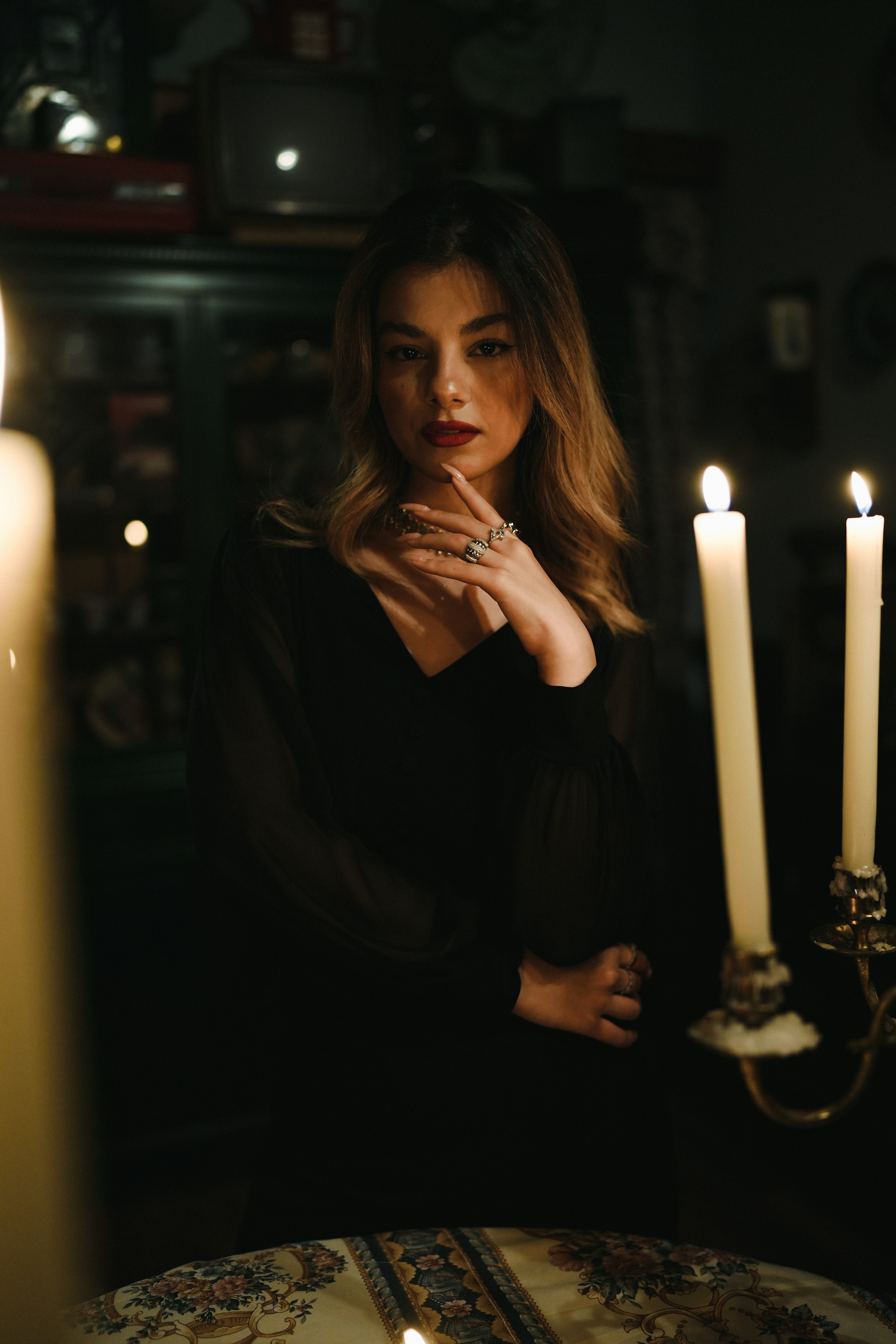 A woman in a black dress posing by candlelight in a dimly lit room