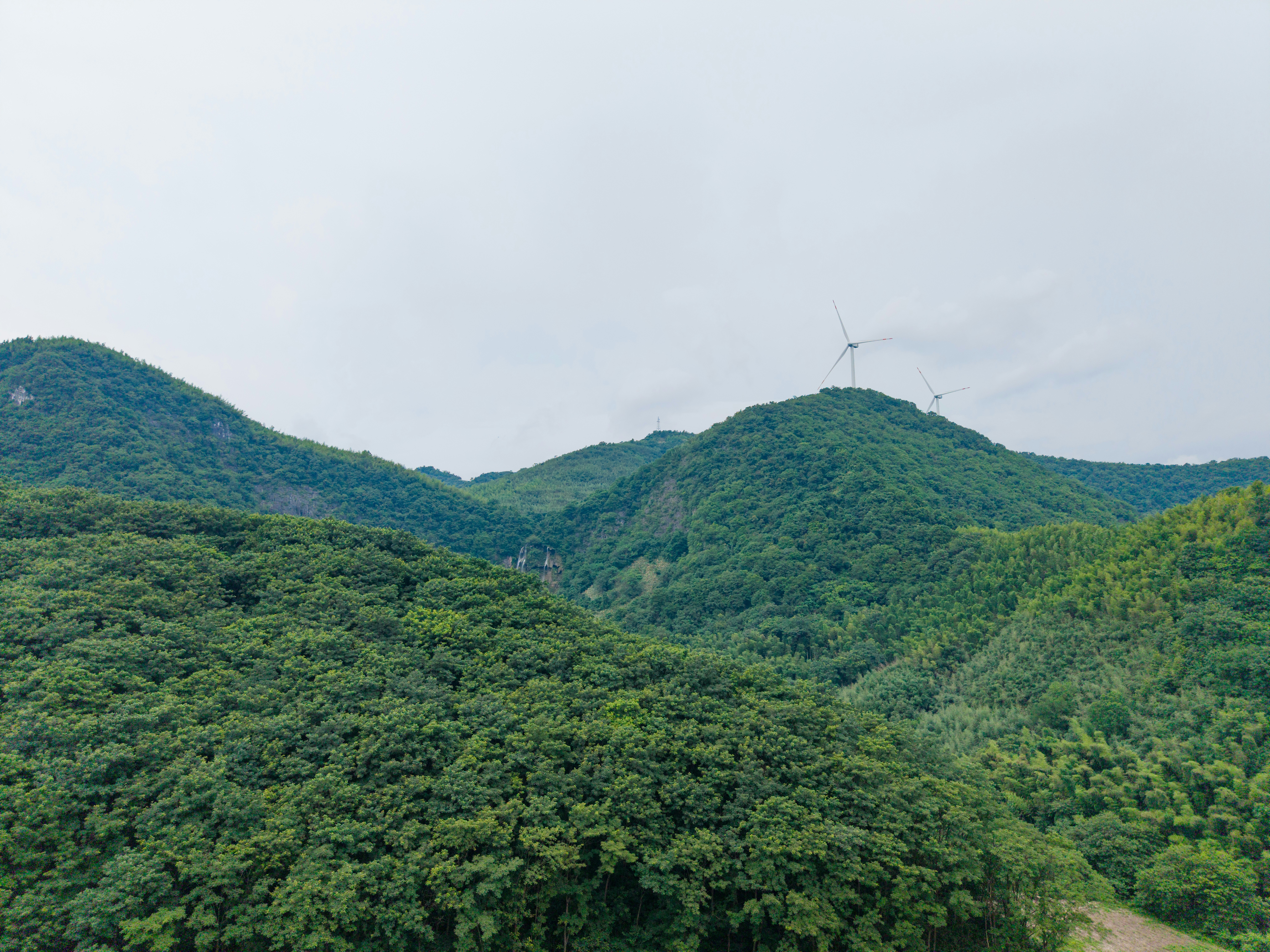 Wind turbines on a lush green mountain ridge under a cloudy sky