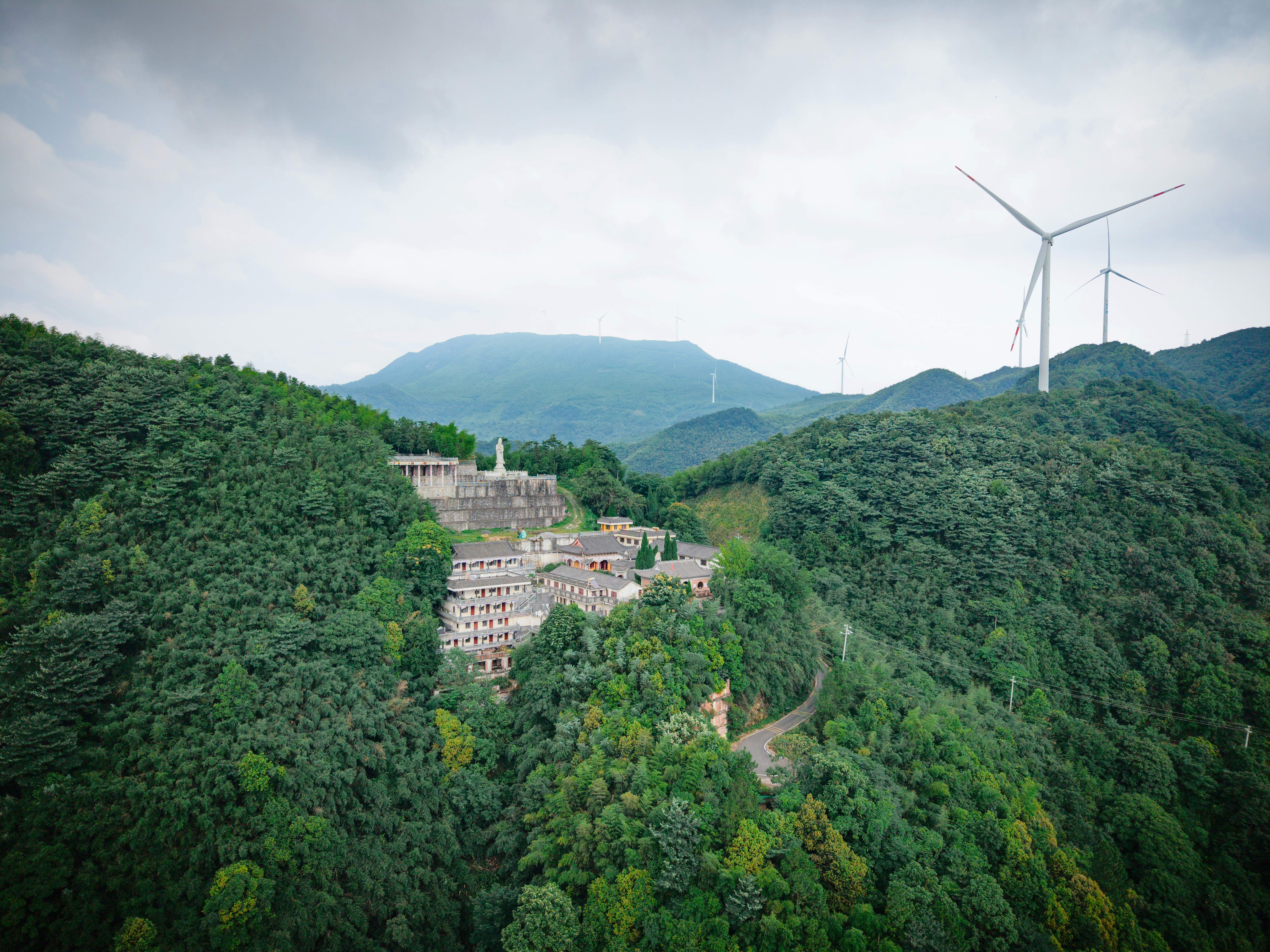 A temple complex nestled in a lush green mountain forest with wind turbines