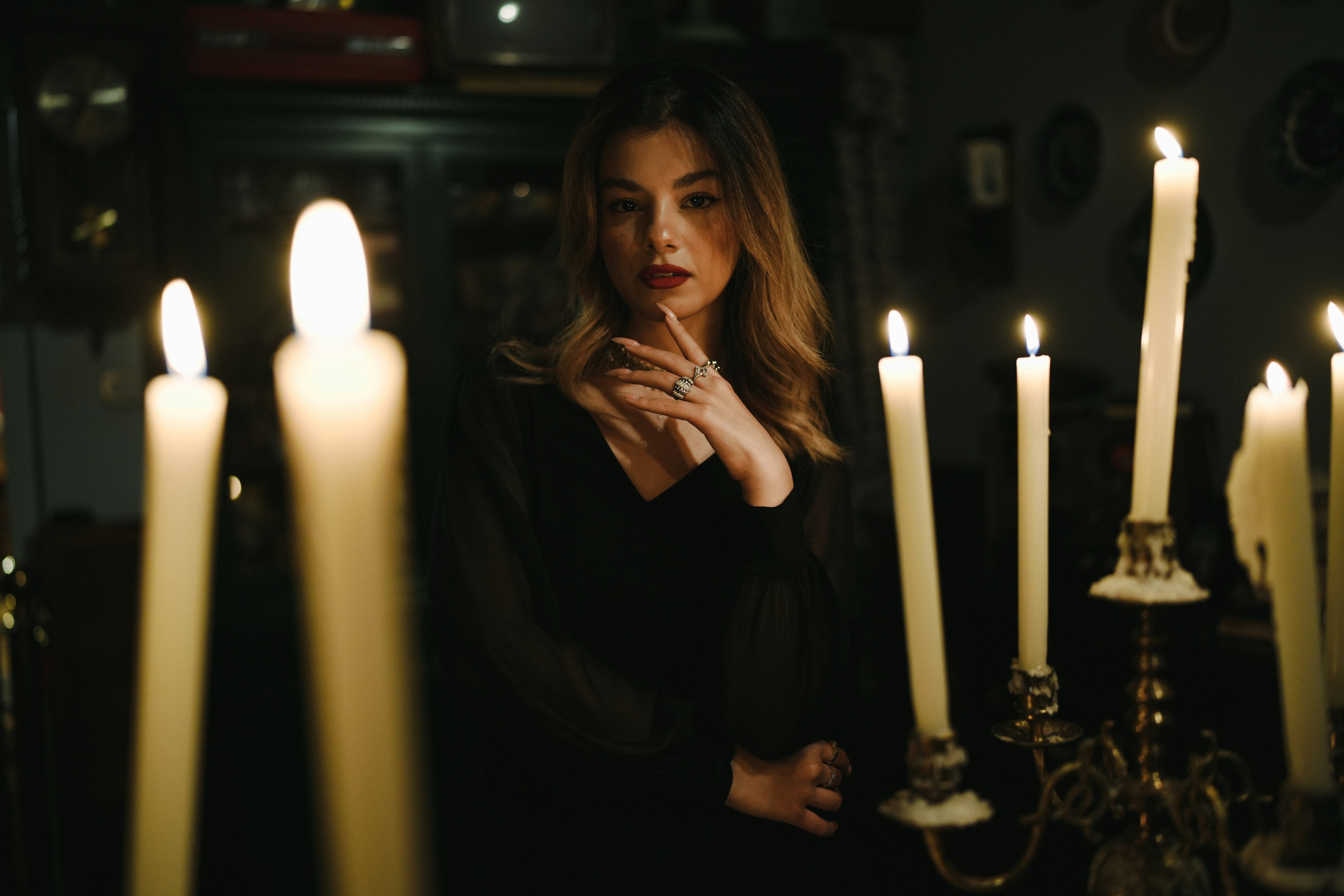A woman in a black dress posing among lit candles in a dark room