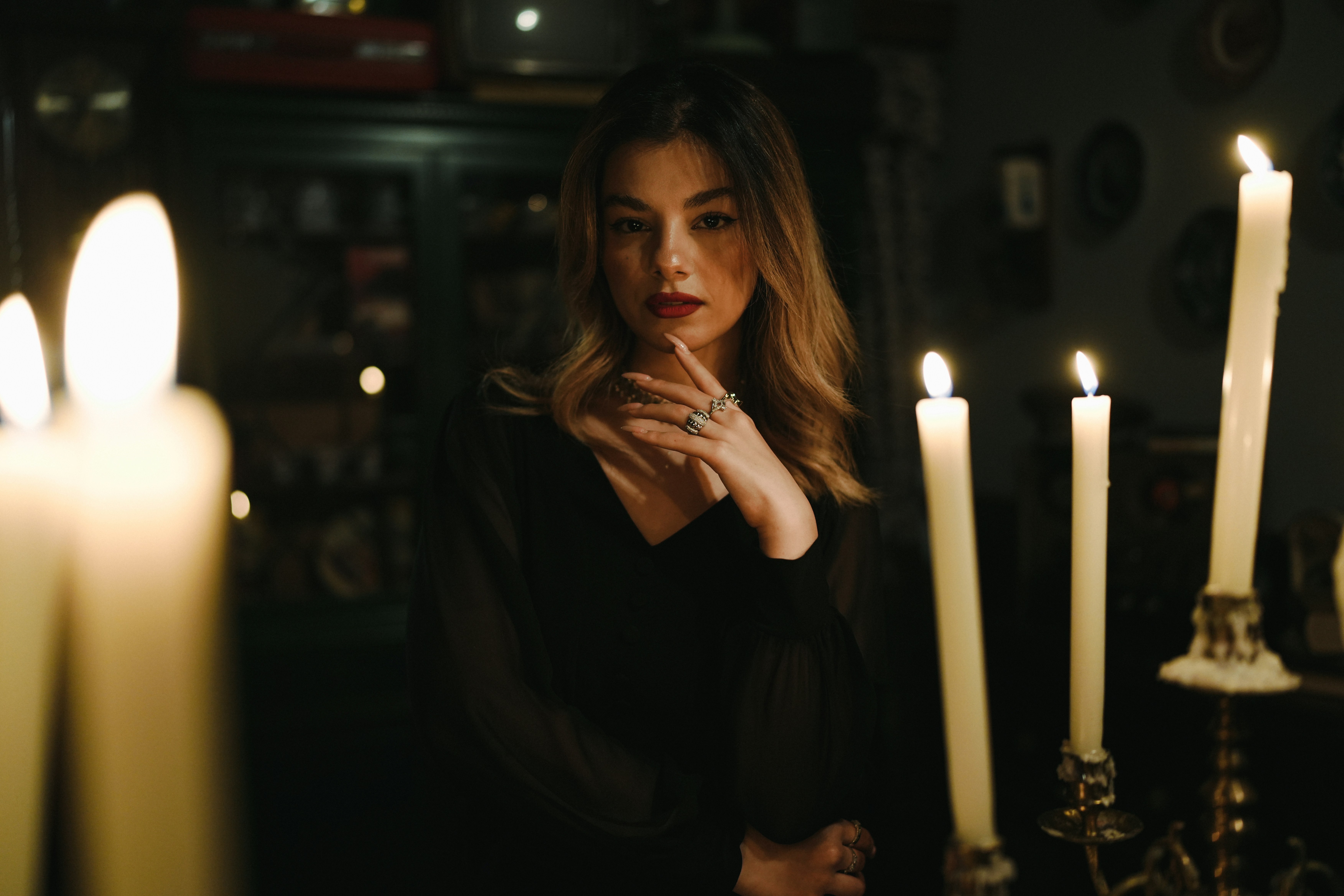 A woman in a black dress with rings, lit by candlelight in a room