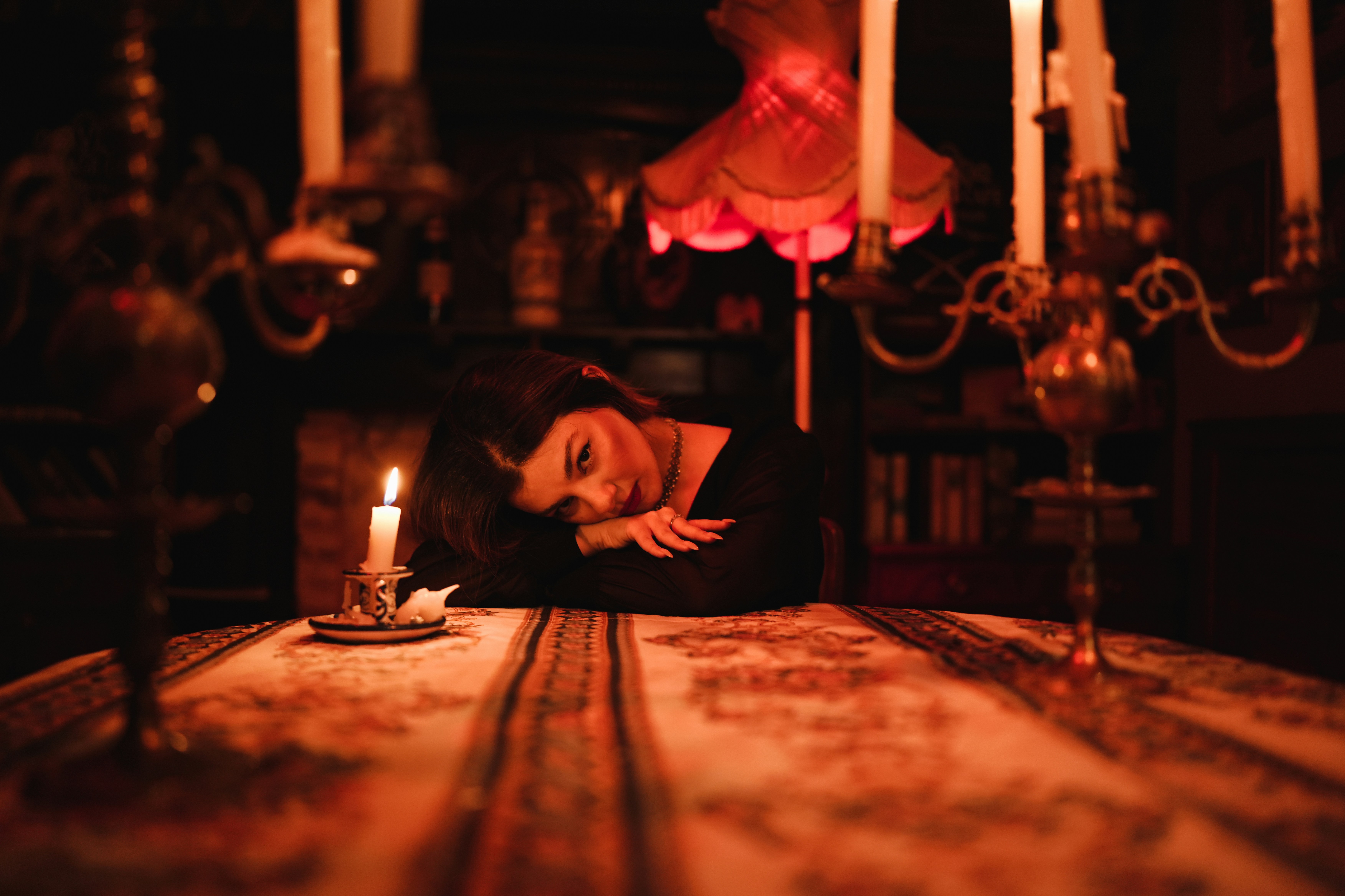A woman in a black dress resting on a table with a lit candle