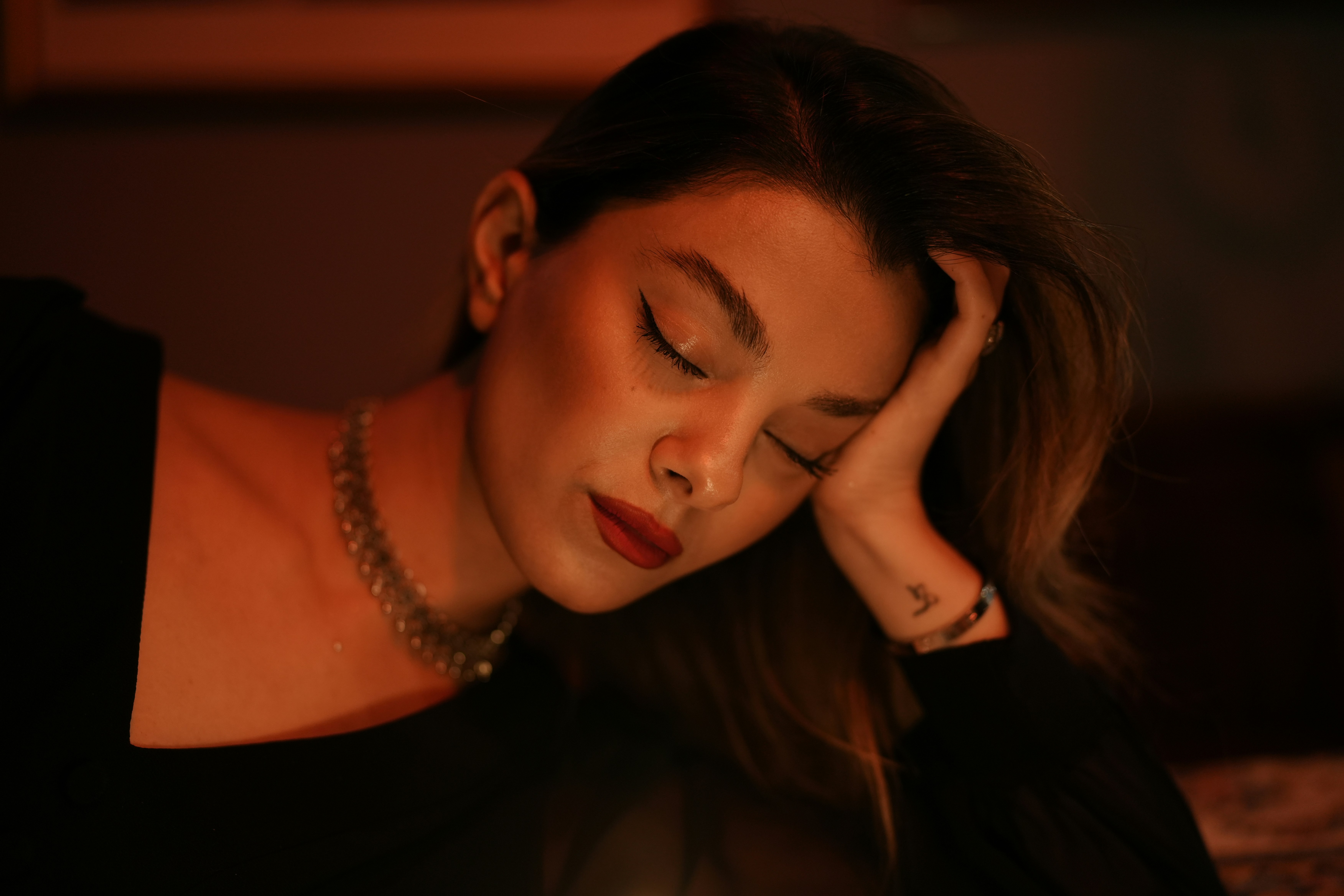 A woman with red lipstick and a necklace resting her head on her hand