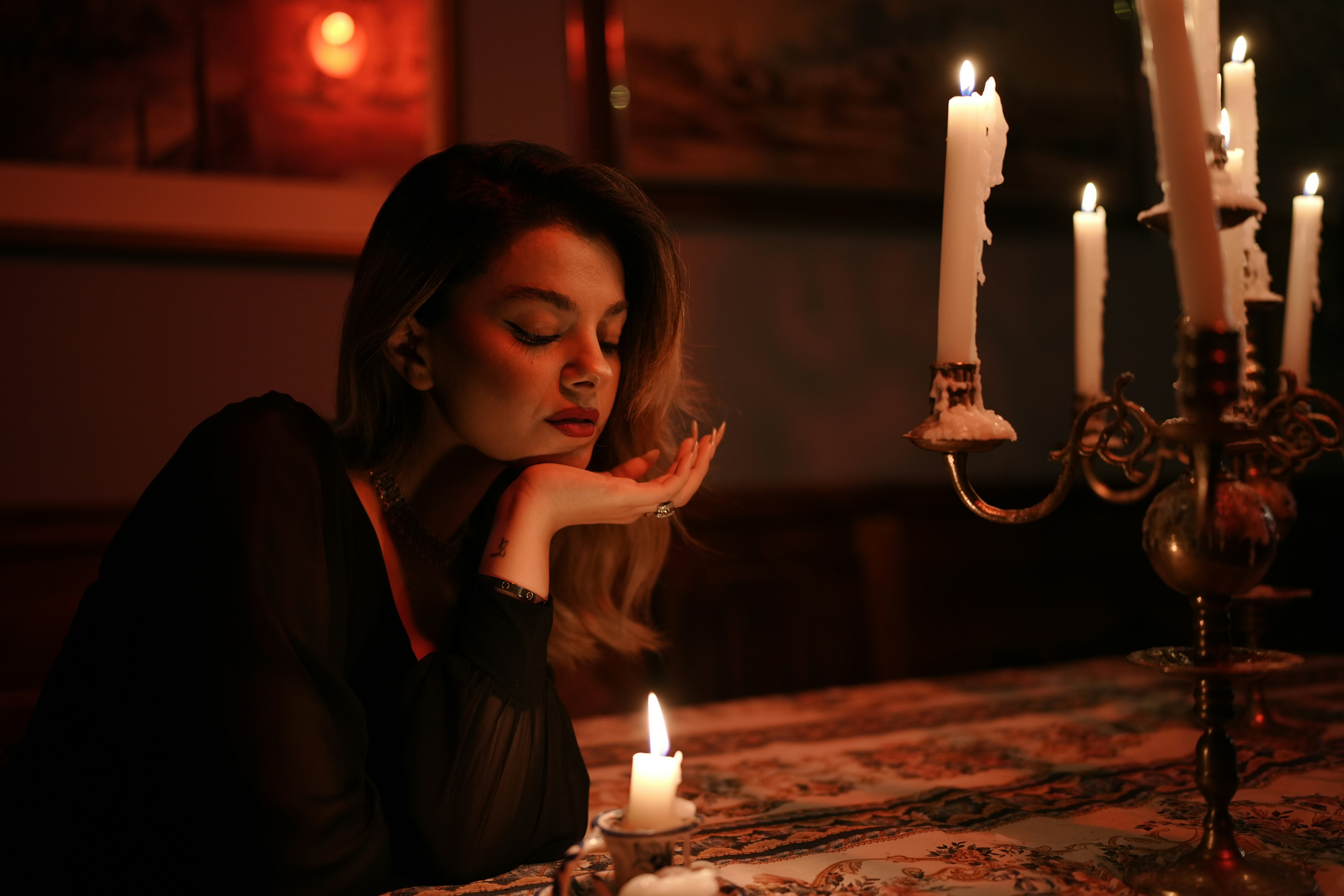 A woman in a black dress resting her chin on her hand by candlelight