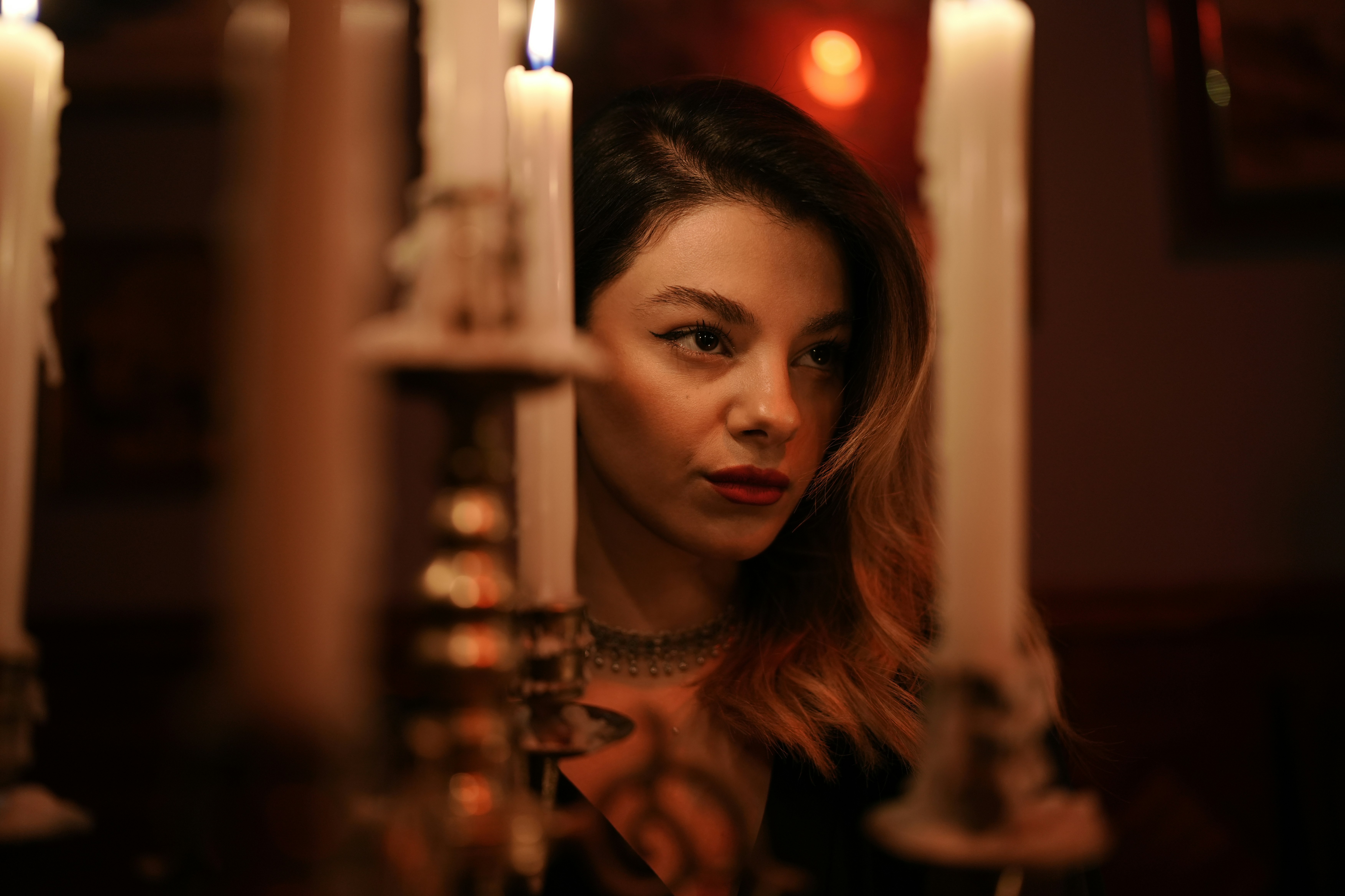 A woman with dark hair behind lit candles in a dimly lit room
