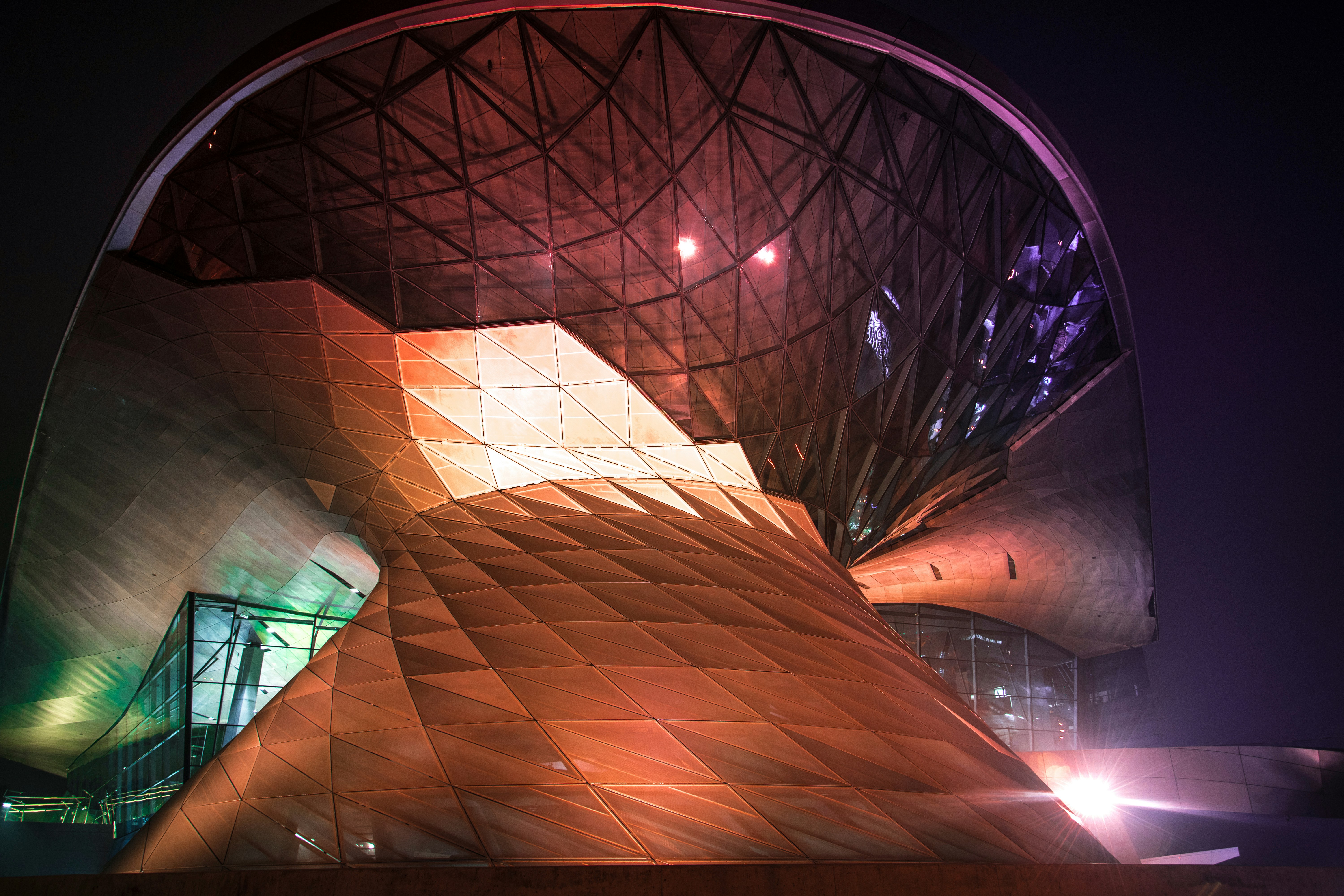 Ein modernes Gebäude mit einer geschwungenen, geometrischen Fassade, die von warmem orangefarbenem Licht erleuchtet wird