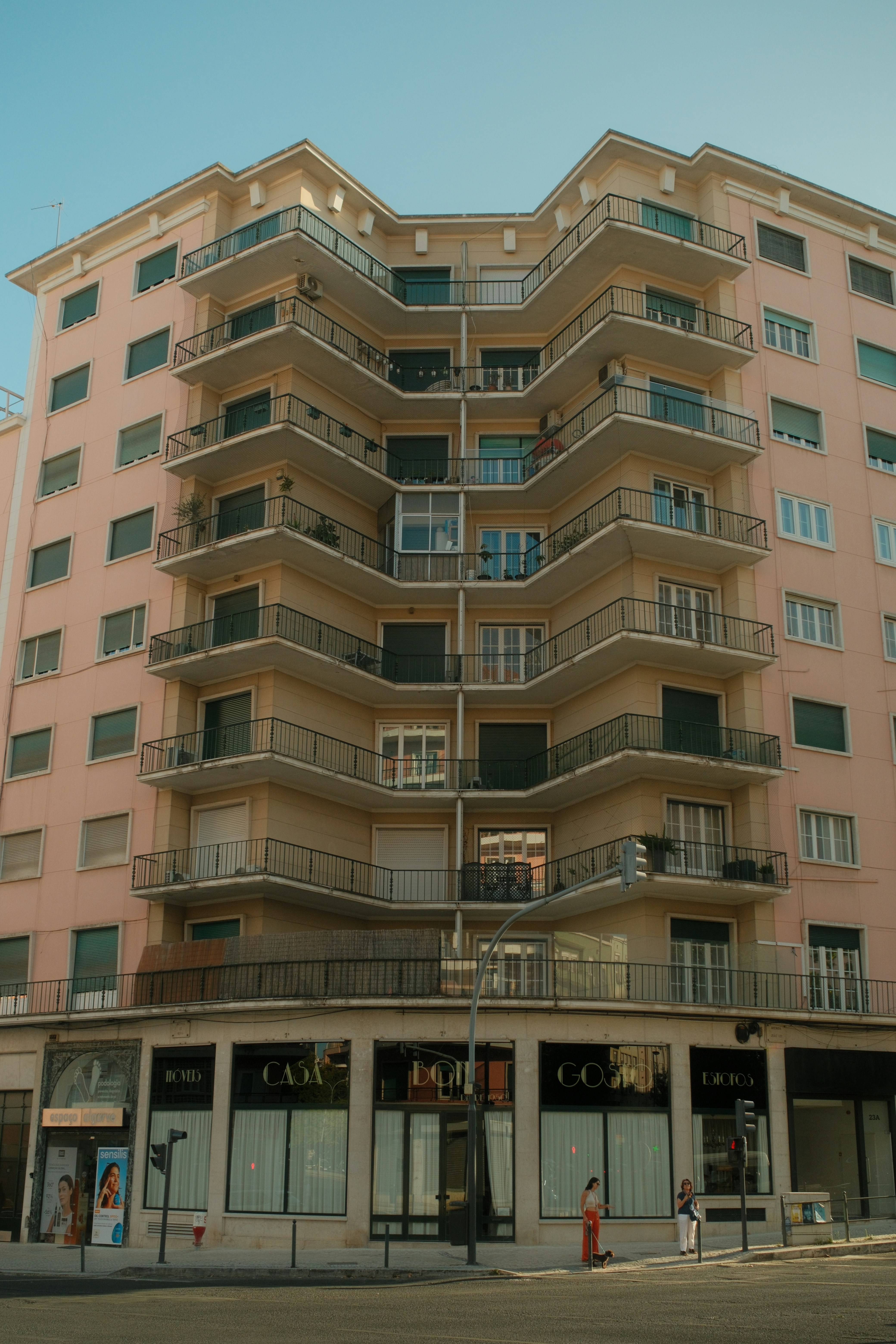Um prédio de apartamentos rosa com varandas em andares acima de uma loja no térreo