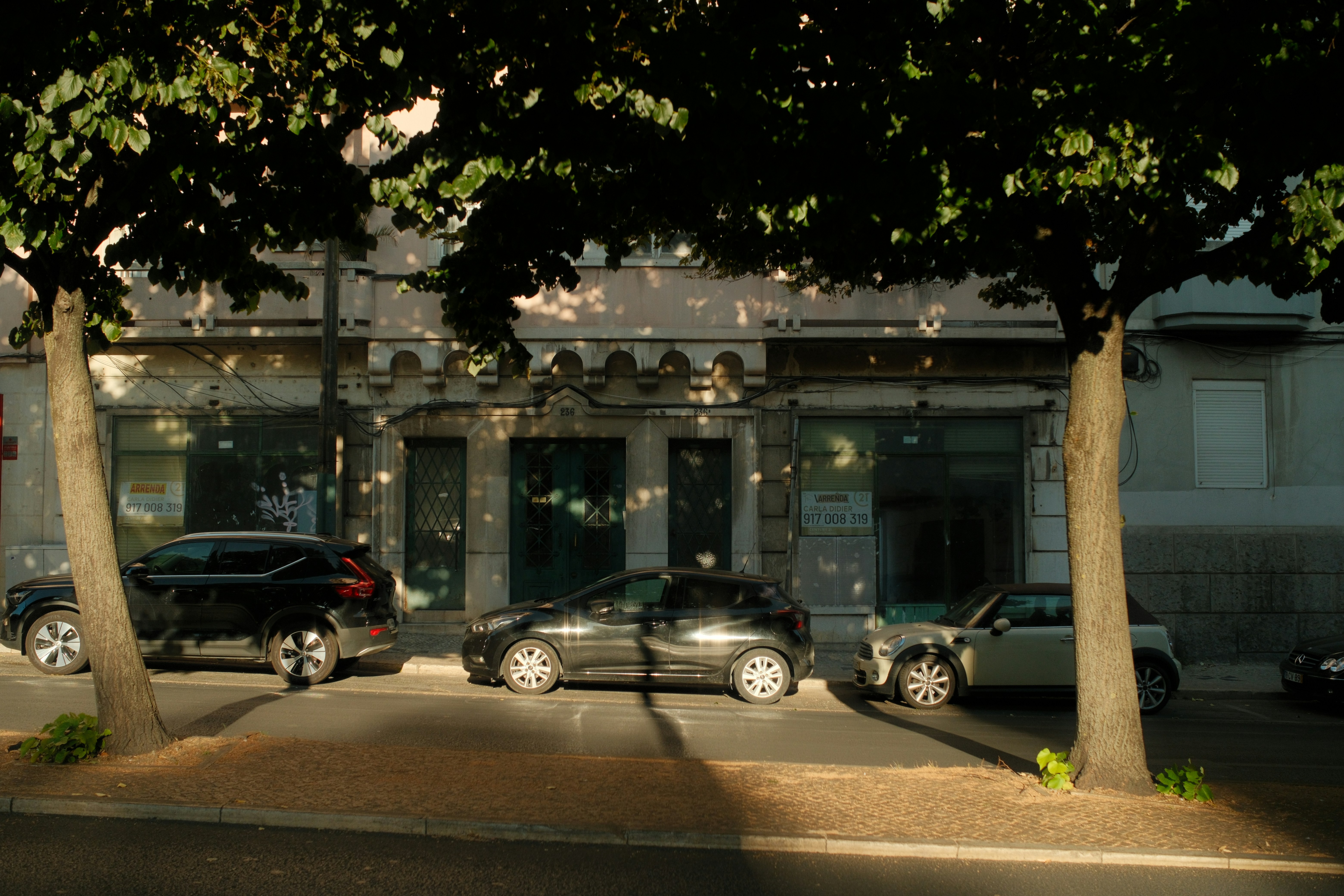 Três carros estacionados em uma rua em frente a um prédio com árvores