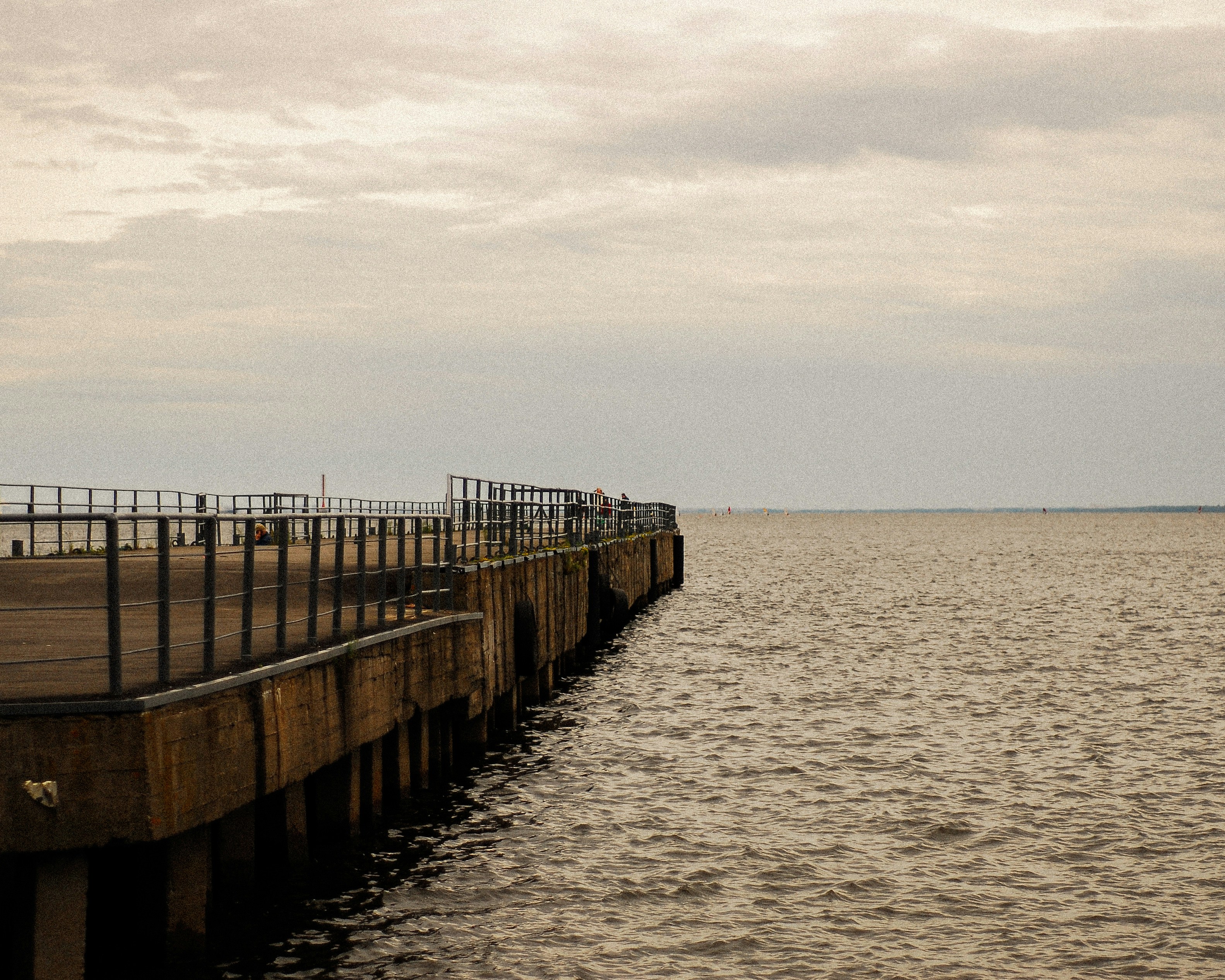 A concrete pier with a metal railing extending into a calm grey sea