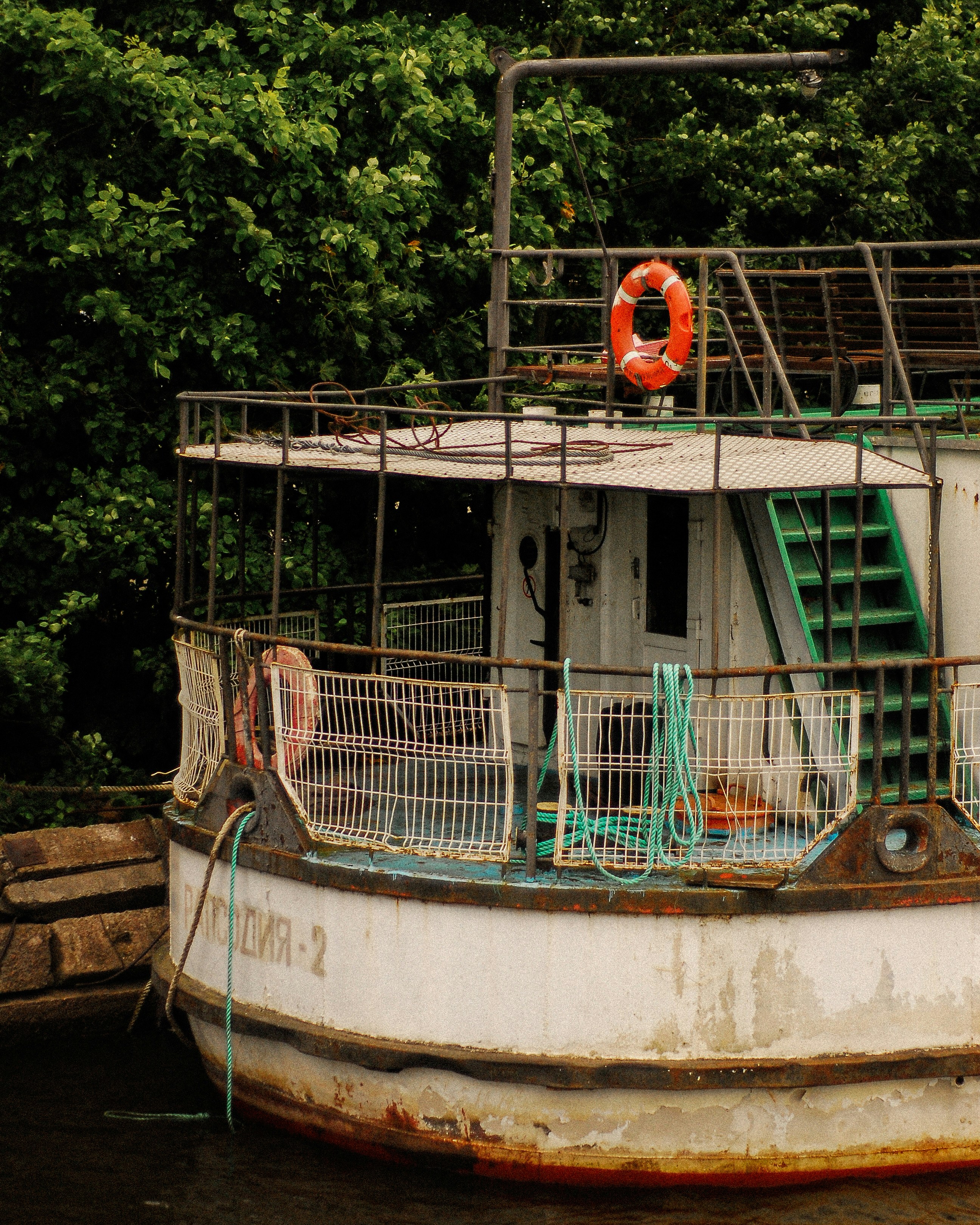 A weathered boat with a life ring and green stairs moored by trees