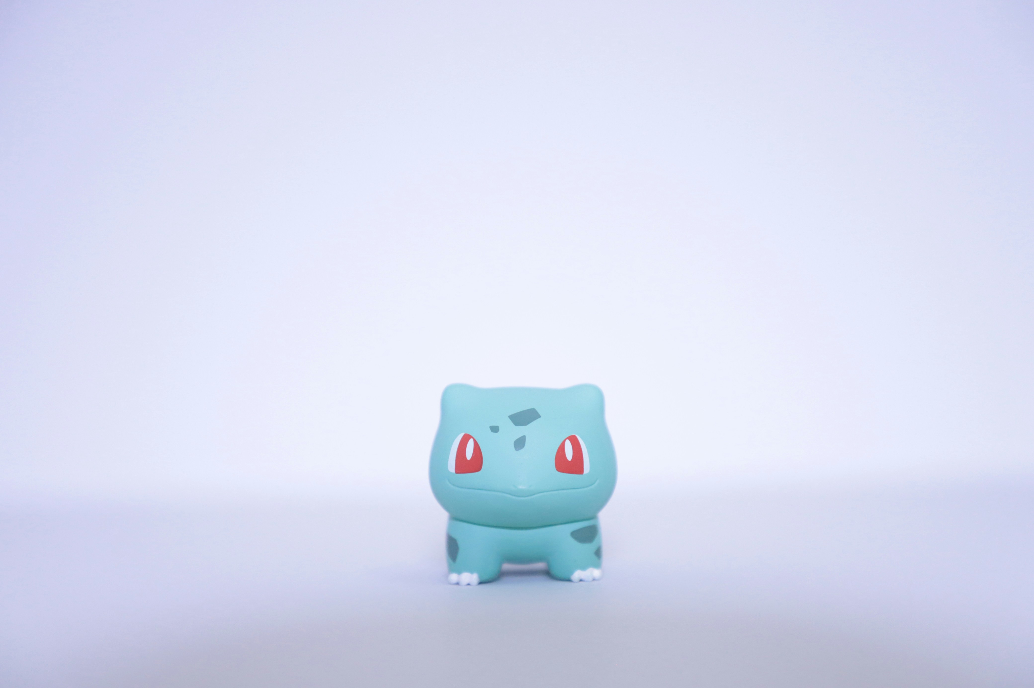 A small teal Bulbasaur figurine with red eyes on a plain white background